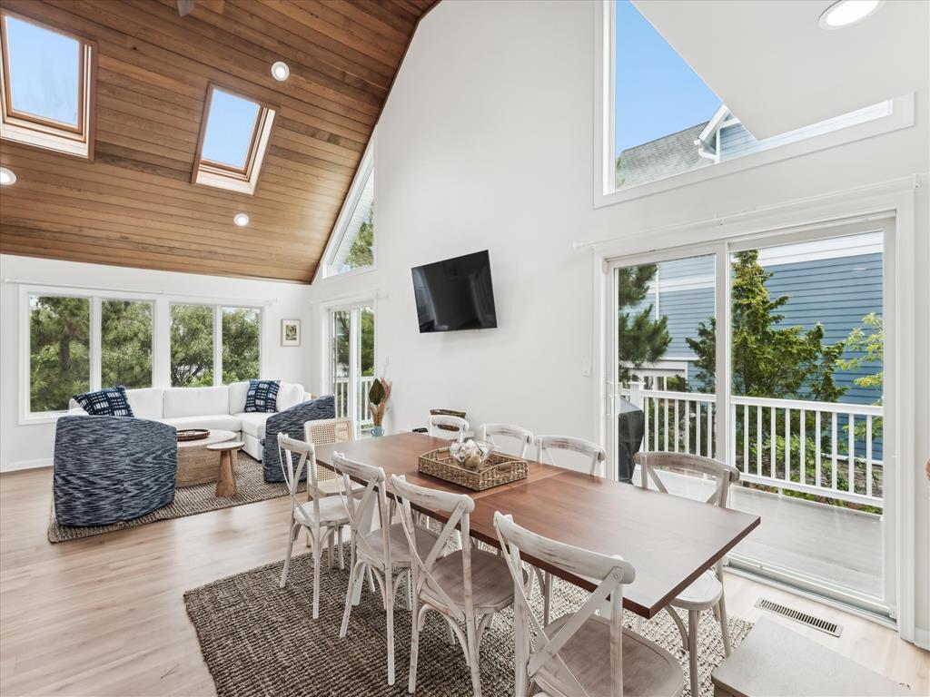 image Vaulted wooden ceiling over dining and living area with windows framing greenery and sunshine.