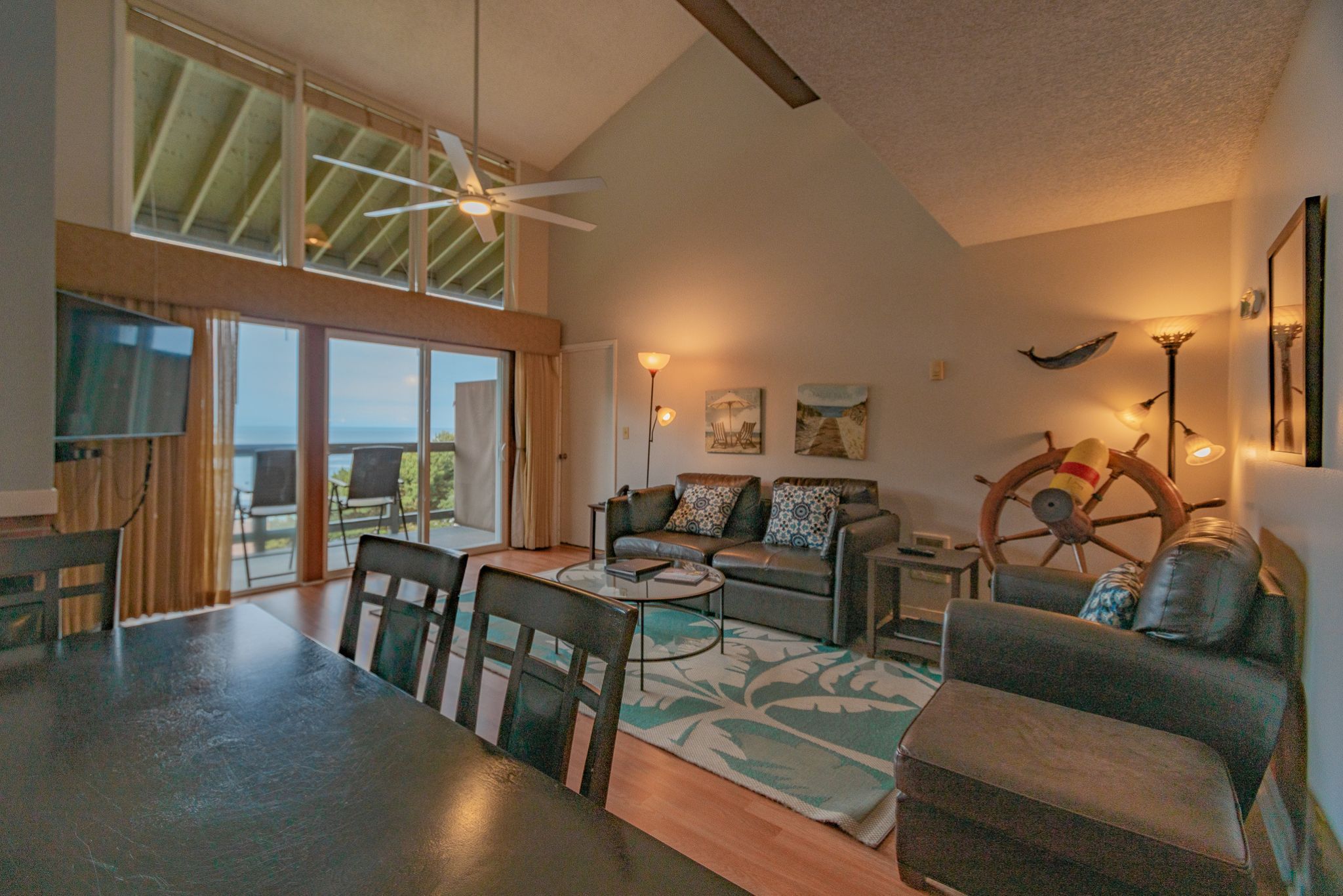 image Spacious living area with vaulted ceiling, leather seating, and sliding doors opening to a balcony with ocean views.