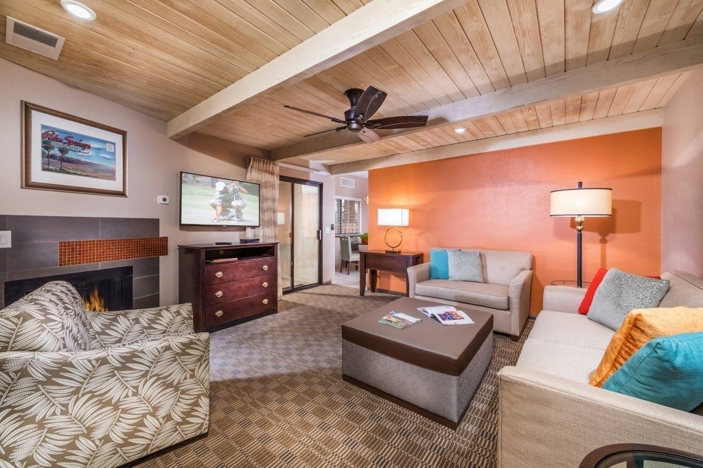 image Enhanced by wooden beams and vibrant accents, the spacious living area invites relaxation with comfortable seating, a fireplace, and a connection to the private patio.