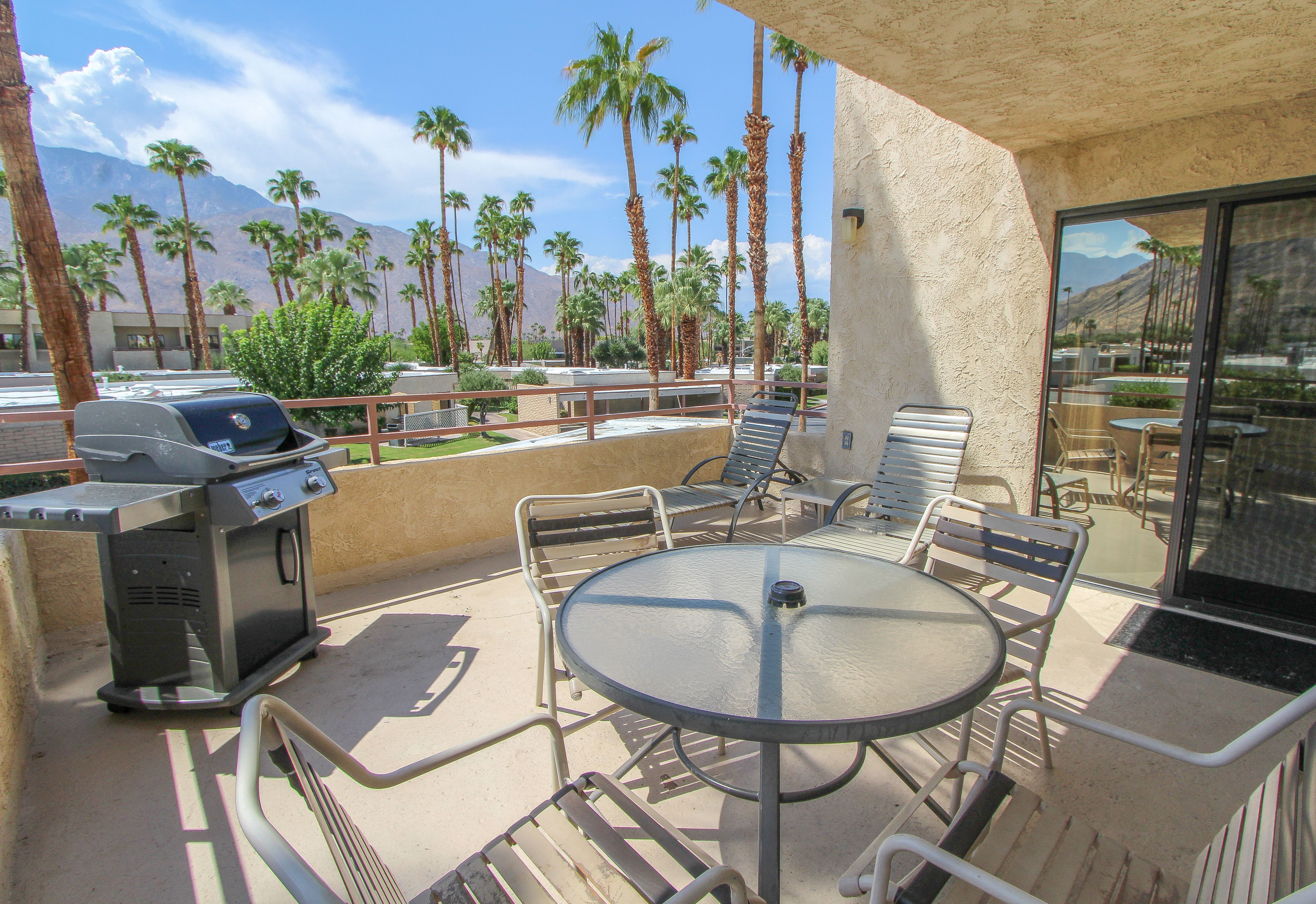 image Enjoy alfresco dining on the spacious balcony equipped with a grill and comfortable seating, all set against a stunning backdrop of palm trees and mountainous views.