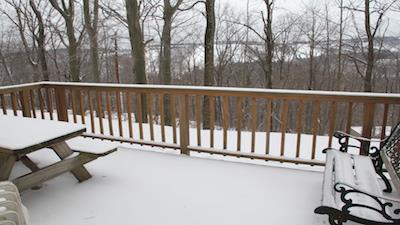 image A serene deck space covered in fresh snow provides a peaceful retreat, framed by tall trees and offering a glimpse of the surrounding landscape.