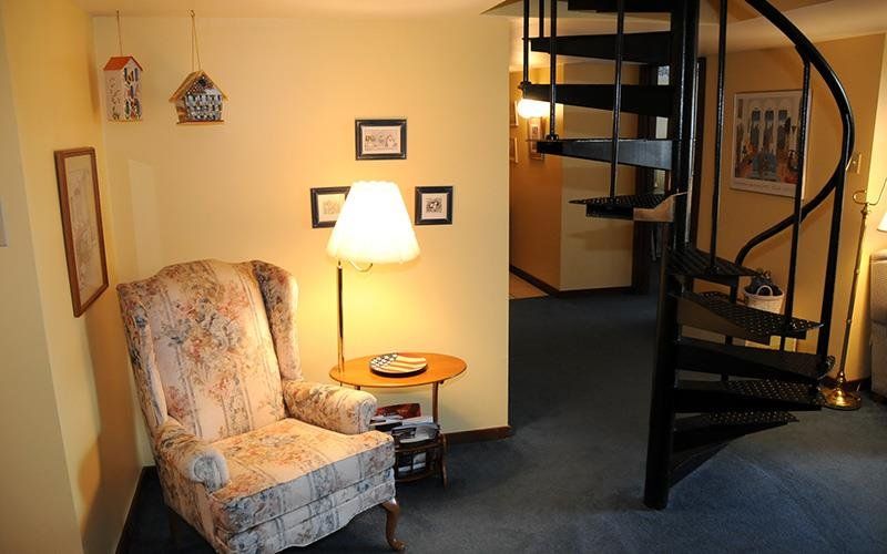 image A charming reading nook with a vintage armchair, illuminated by a warm lamp, alongside a stylish spiral staircase.