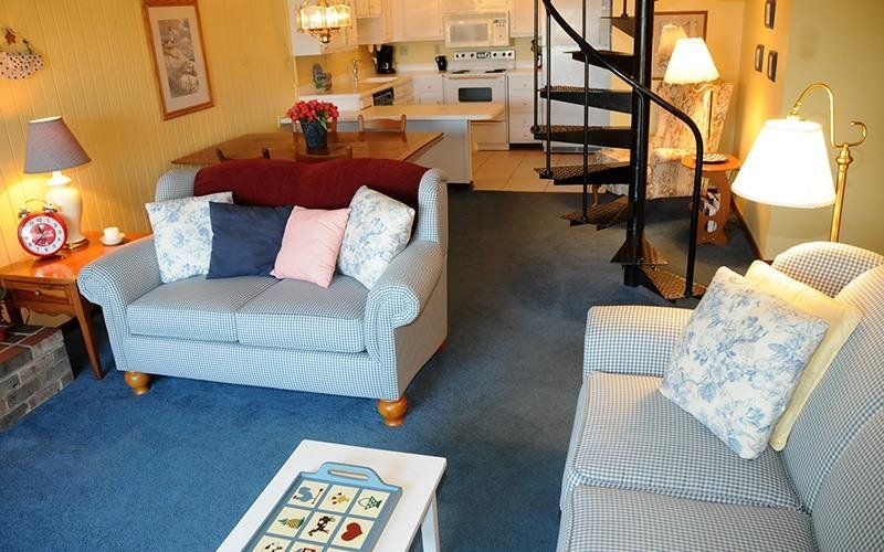 image The cozy living area features comfortable seating with a spiral staircase leading to the loft and a warm, inviting kitchen in the background.