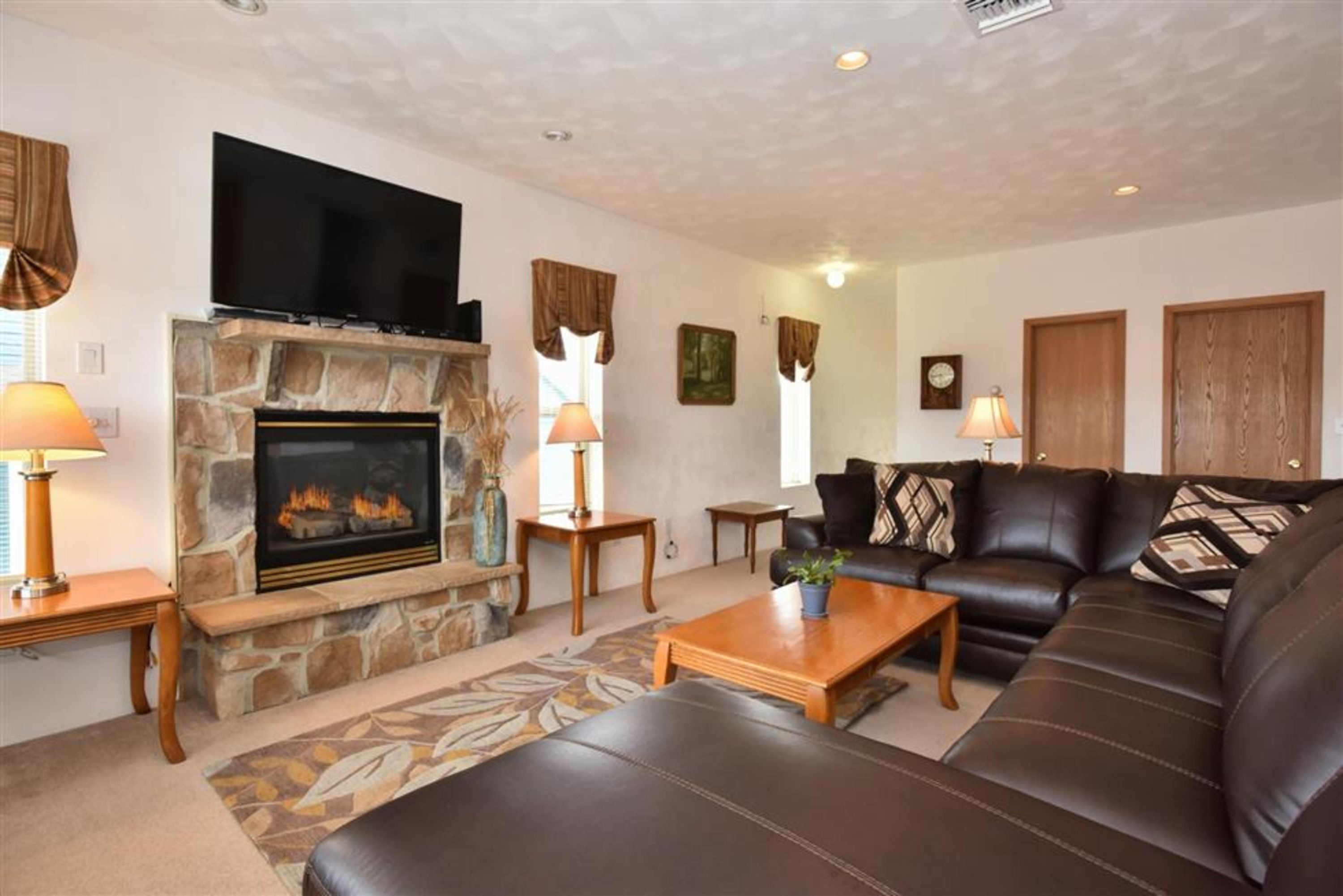 image Spacious seating area featuring a stone fireplace, flat-screen TV, and comfortable leather sofas.