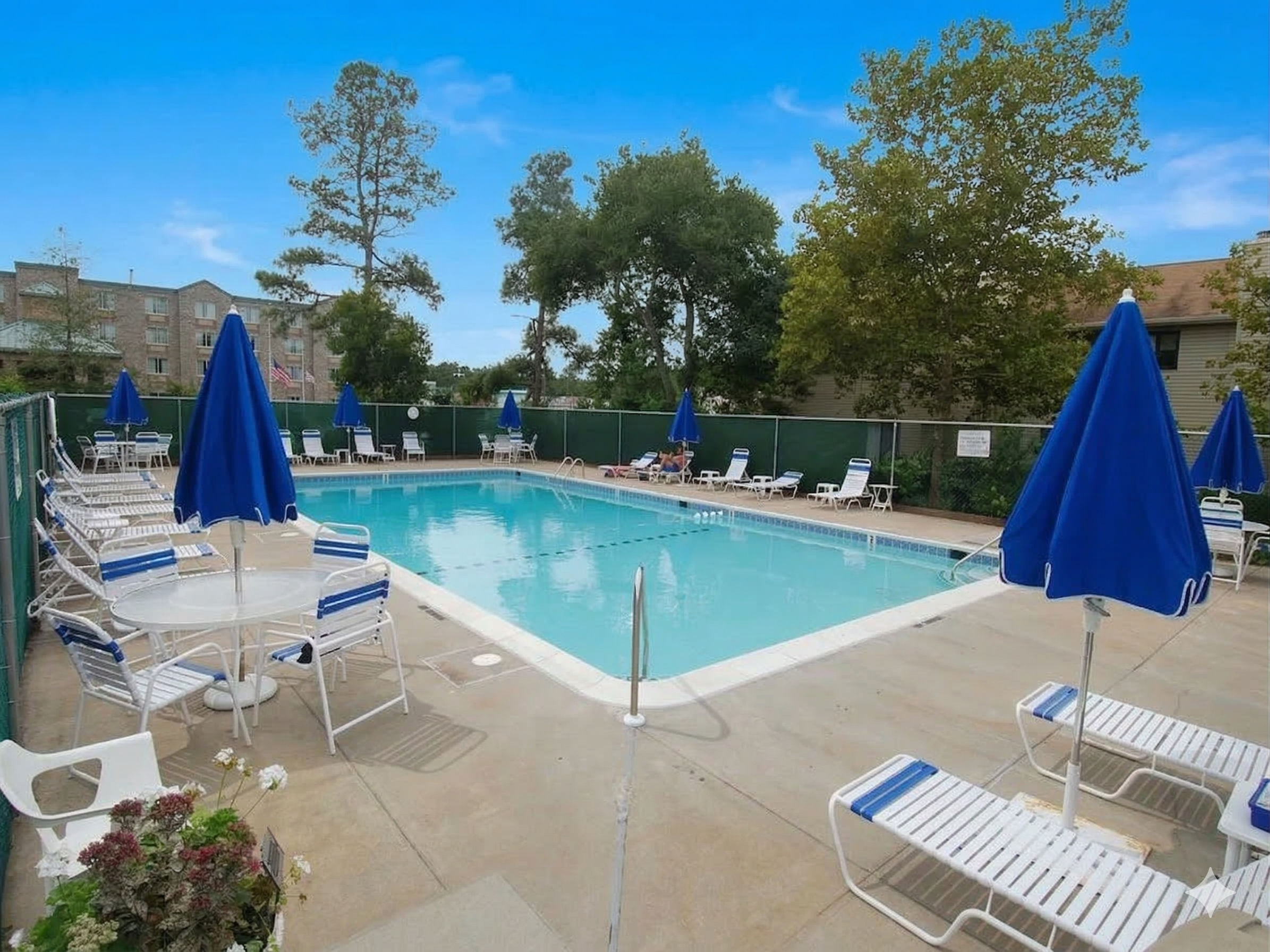 image Relax by the community pool, surrounded by loungers and vibrant blue umbrellas, perfect for sunny days.