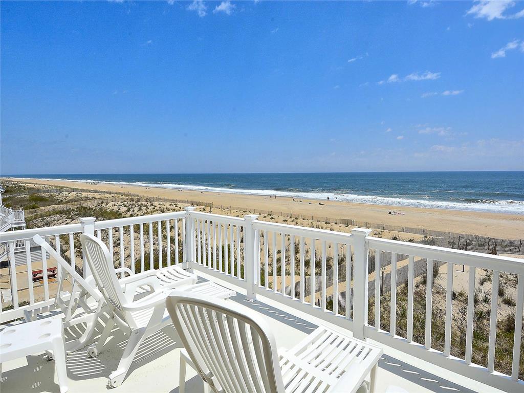 image Oceanfront balcony with white patio chairs and a panoramic view of the beach and water.
