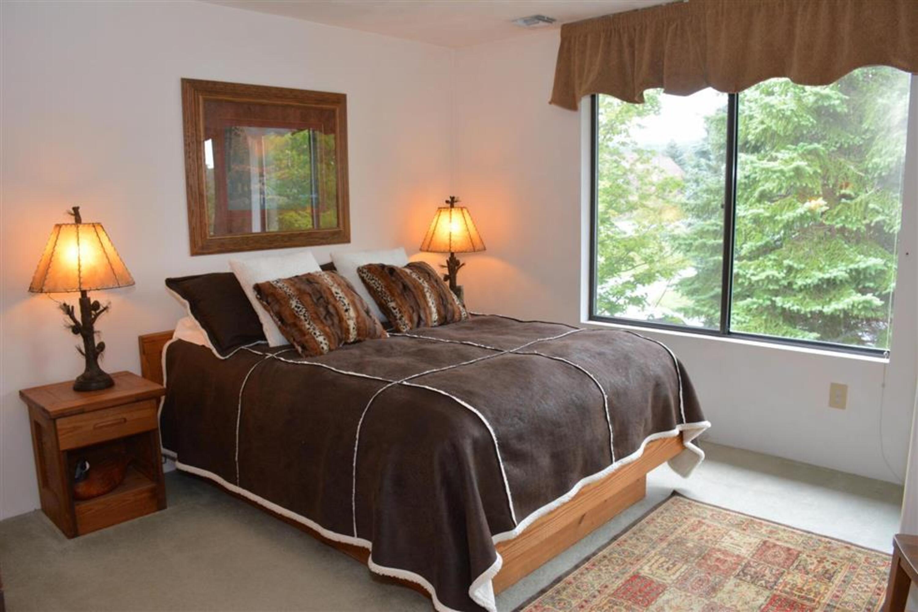 image Main-level bedroom with queen bed, soft linens, and a large window offering natural light and forest views.