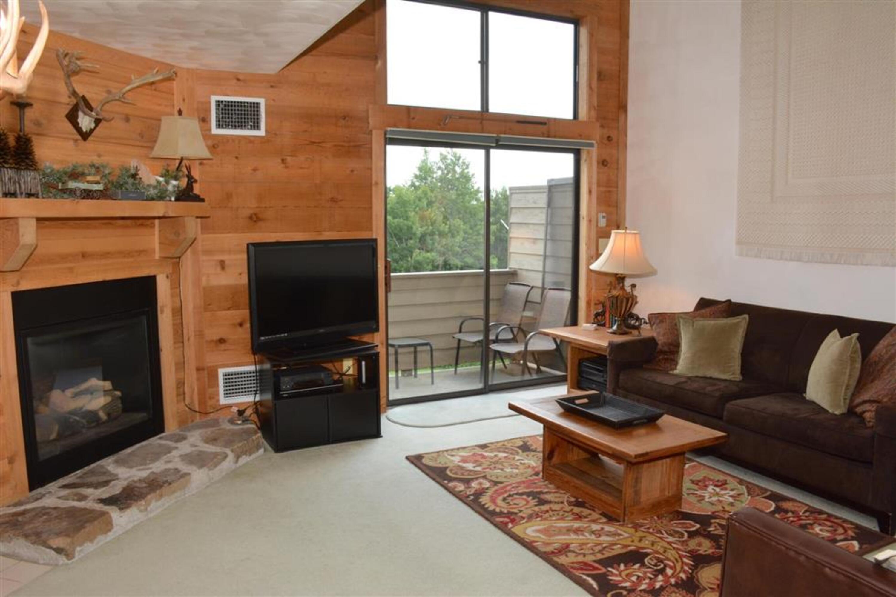 image Inviting living room with gas fireplace, vaulted ceilings, and access to a private woodland-view deck.