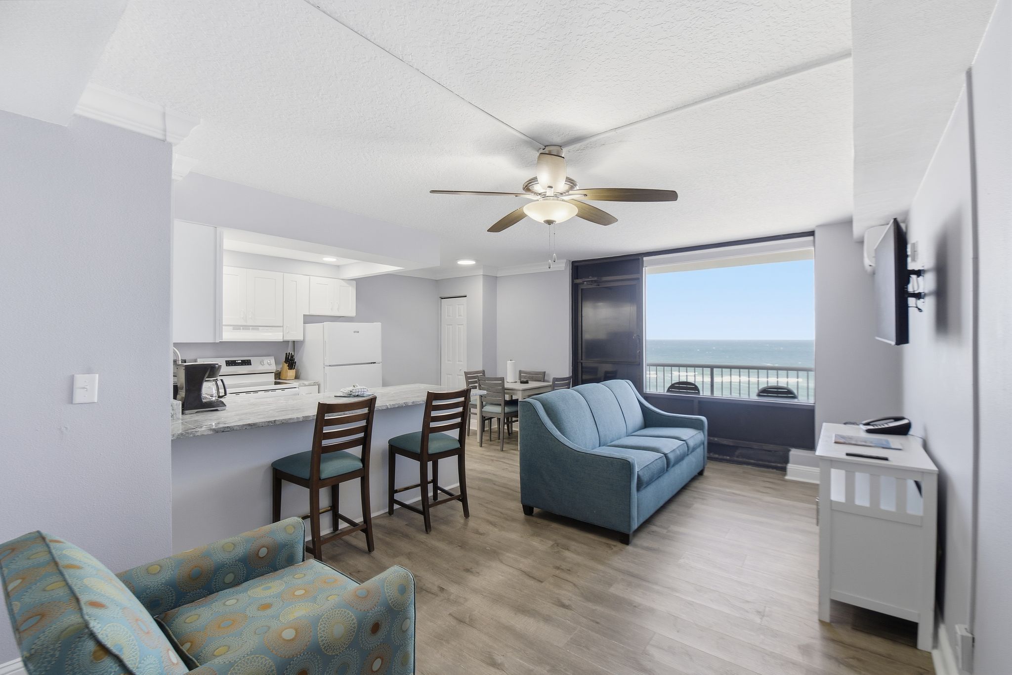 image The spacious living area boasts plush, blue sofas nestled against large windows, inviting natural light and breathtaking ocean views, perfect for relaxation after a day at the beach.