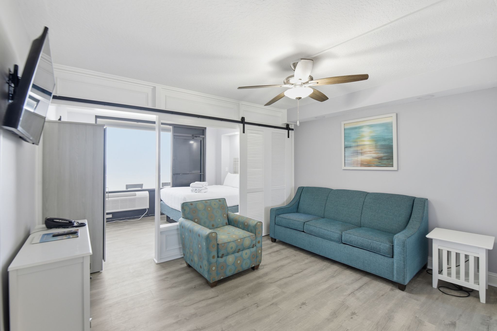 image The spacious living area features a cozy teal couch and armchair, styled with a modern aesthetic, offering a welcoming retreat with natural light streaming in from the adjoining sleeping space.