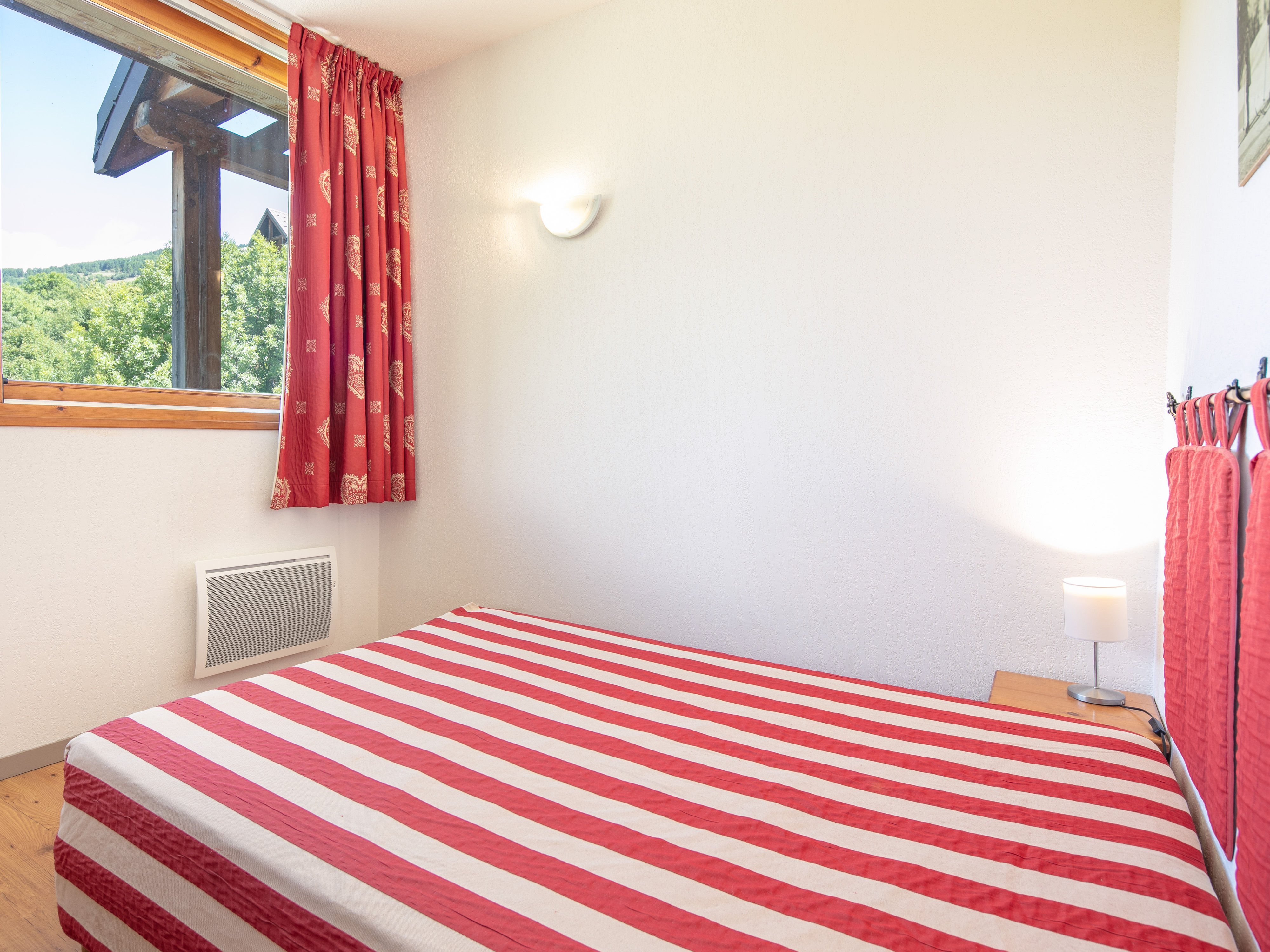 image Comfortable bedroom with red-striped bedding and mountain light streaming through the window.