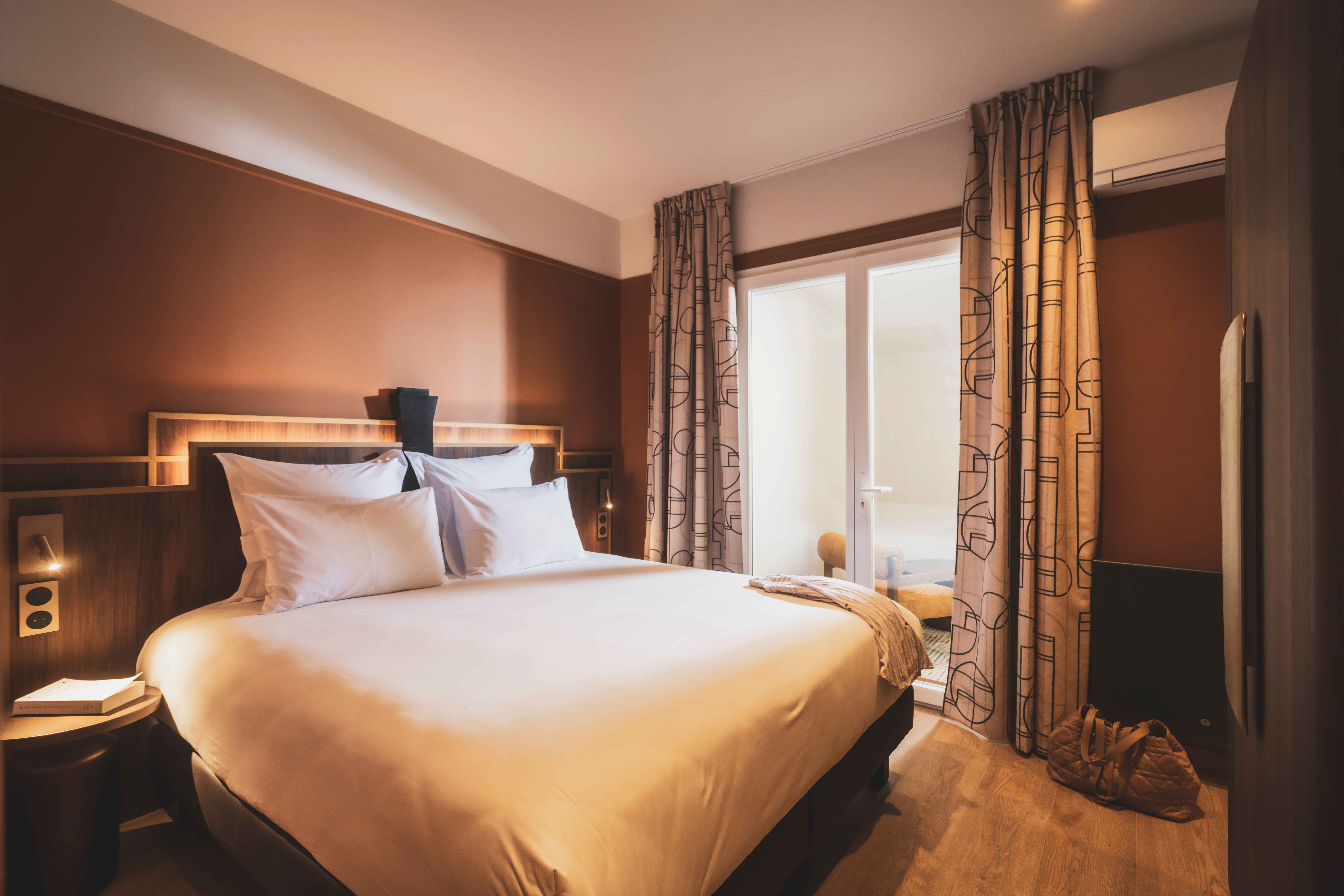 image Cozy and elegant, this sunlit bedroom blends Art-Deco lines with soft tones for a restful night’s sleep.