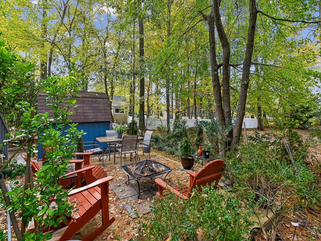 image Outdoor seating area with various plants, a firepit, and a blue storage shed in the distance