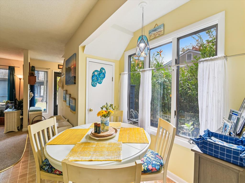 image Sunlit dining area with large windows, coastal artwork on the wall, and green views outside