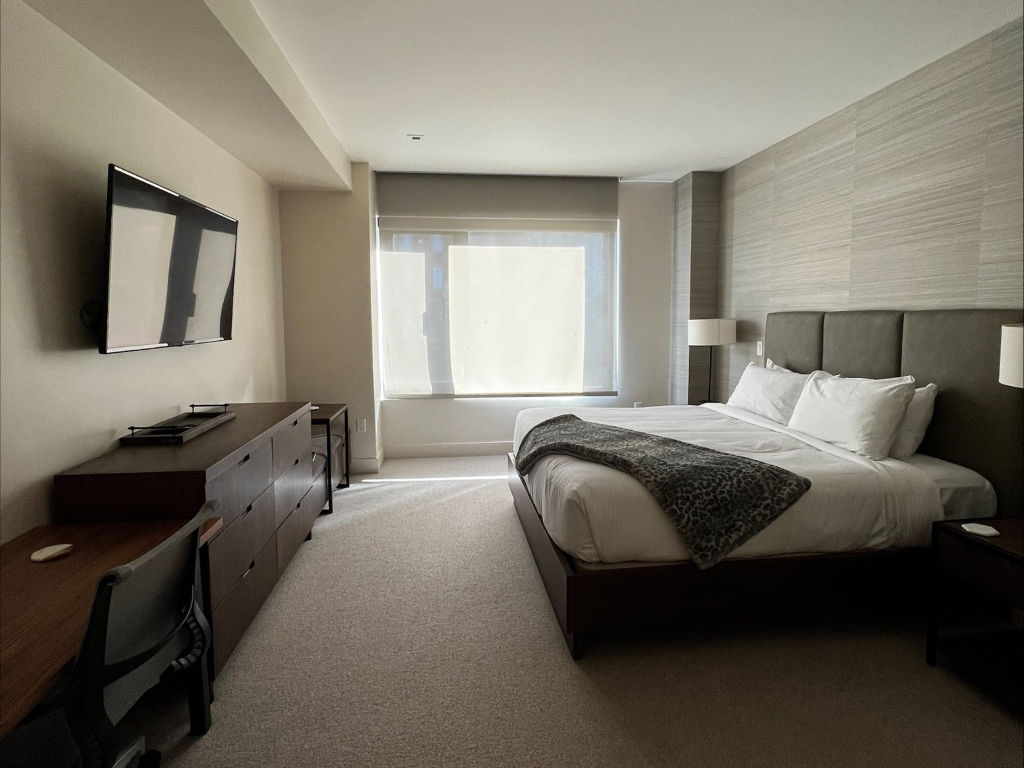 image The spacious bedroom features a king-size bed, a sleek television mounted on the wall, and large windows that allow natural light to fill the room.