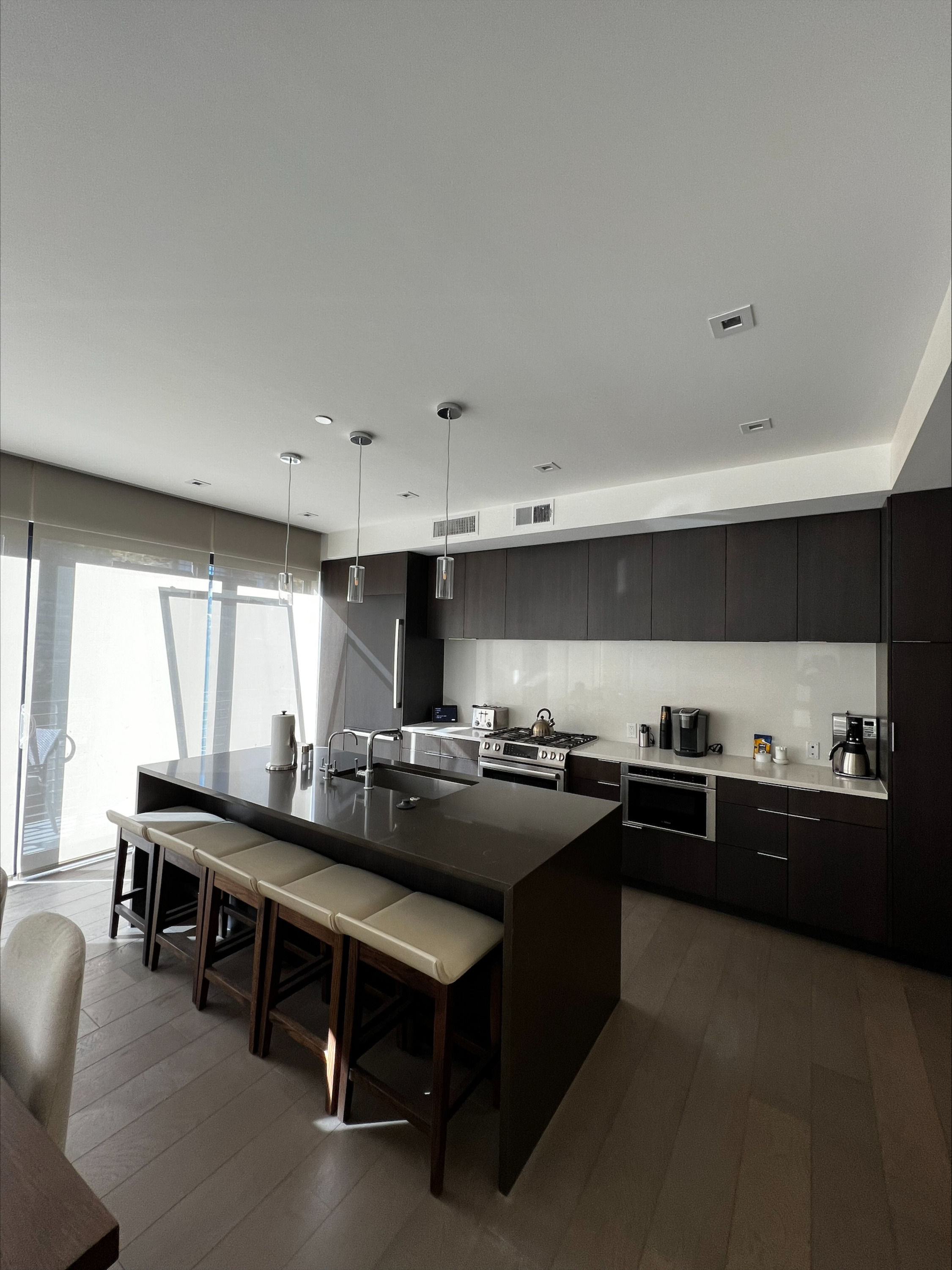 image The contemporary kitchen is equipped with sleek dark cabinetry, high-end appliances, and a large island with seating for casual dining.