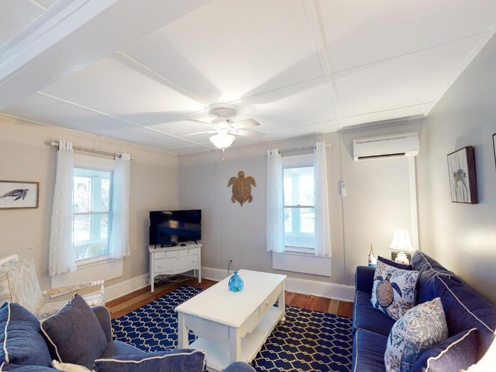 image The cozy living room features a blue sectional sofa, a coffee table, and a TV, illuminated by natural light from the dual windows with white curtains.