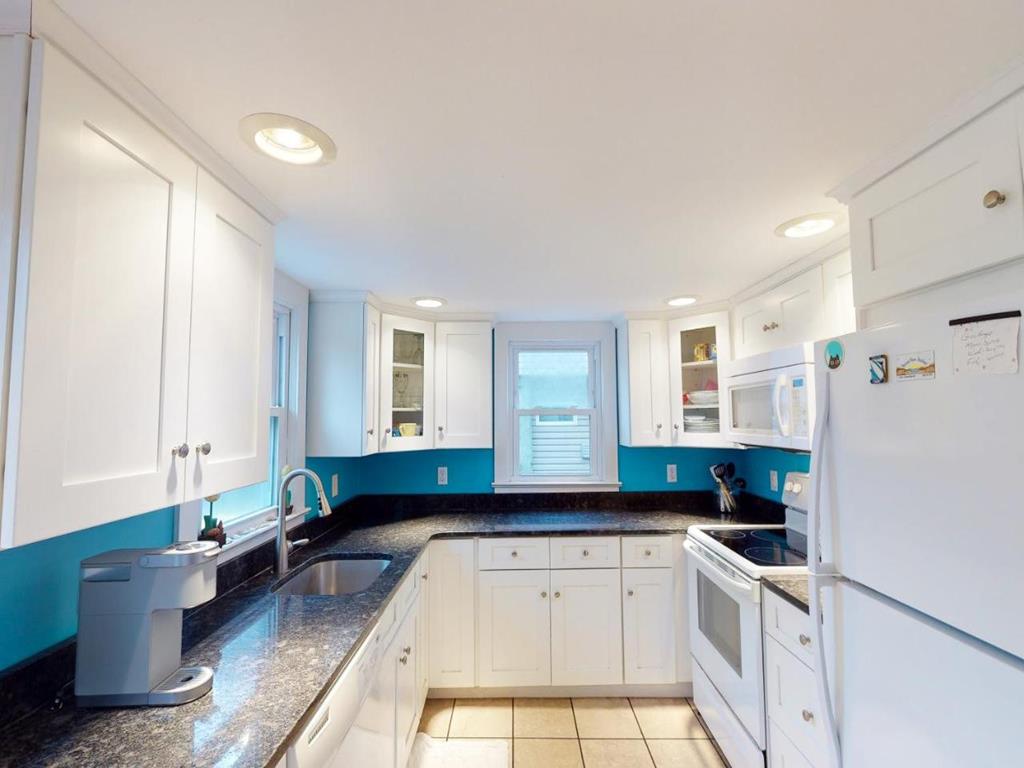 image The kitchen is modern with white cabinetry, black countertops, and stainless steel appliances, accented by vibrant turquoise walls that add a fresh touch.