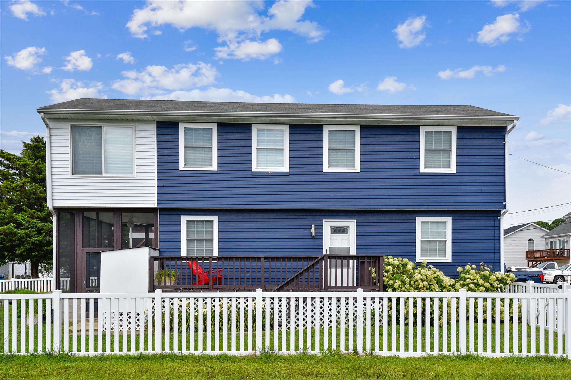 image Blue-and-white exterior with lush front landscaping, white picket fence, and steps leading up to the screened porch
