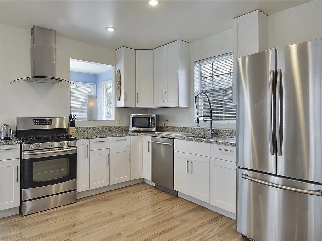 image Well-equipped kitchen with double sink, gas stove, and built-in appliances set in white cabinetry.