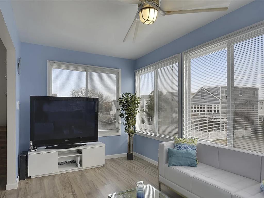 image Airy living room with large windows, a TV stand, decorative plants, and ceiling fan.