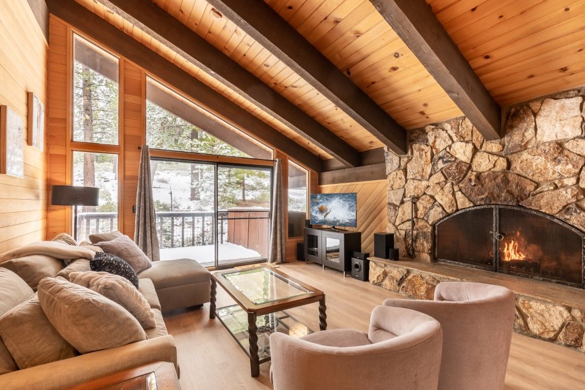 image Cozy living room with a stunning stone fireplace, large windows, and views of the snow-covered outdoors.