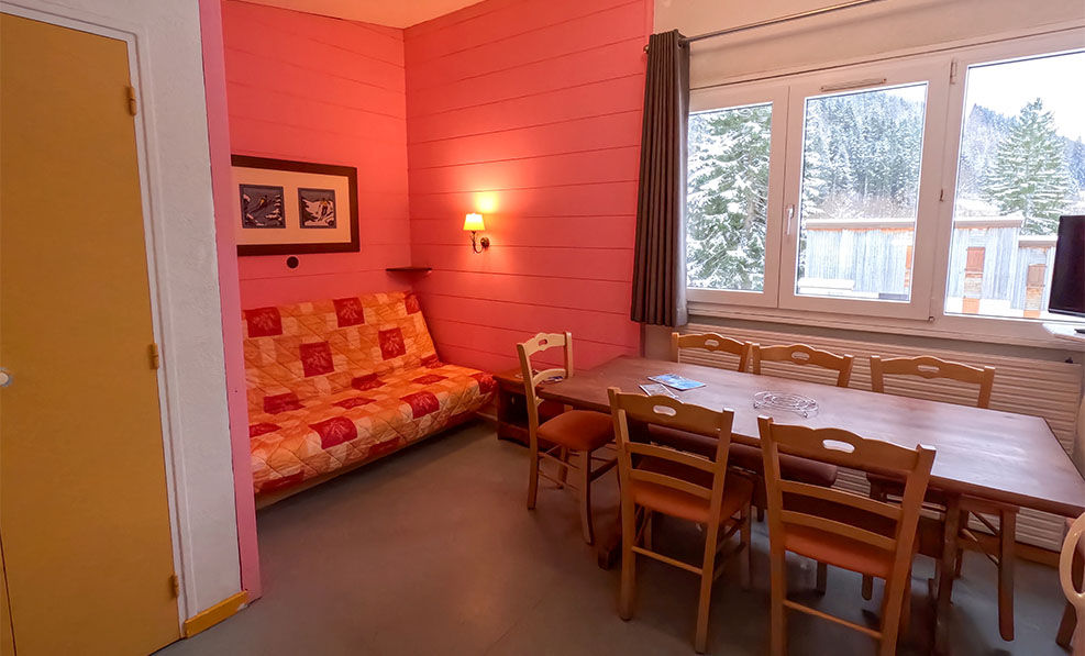 image The cozy living area, adorned with warm mountain décor and a vibrant pink wall, invites family gatherings and relaxation, featuring a comfortable sofa and a large dining table.