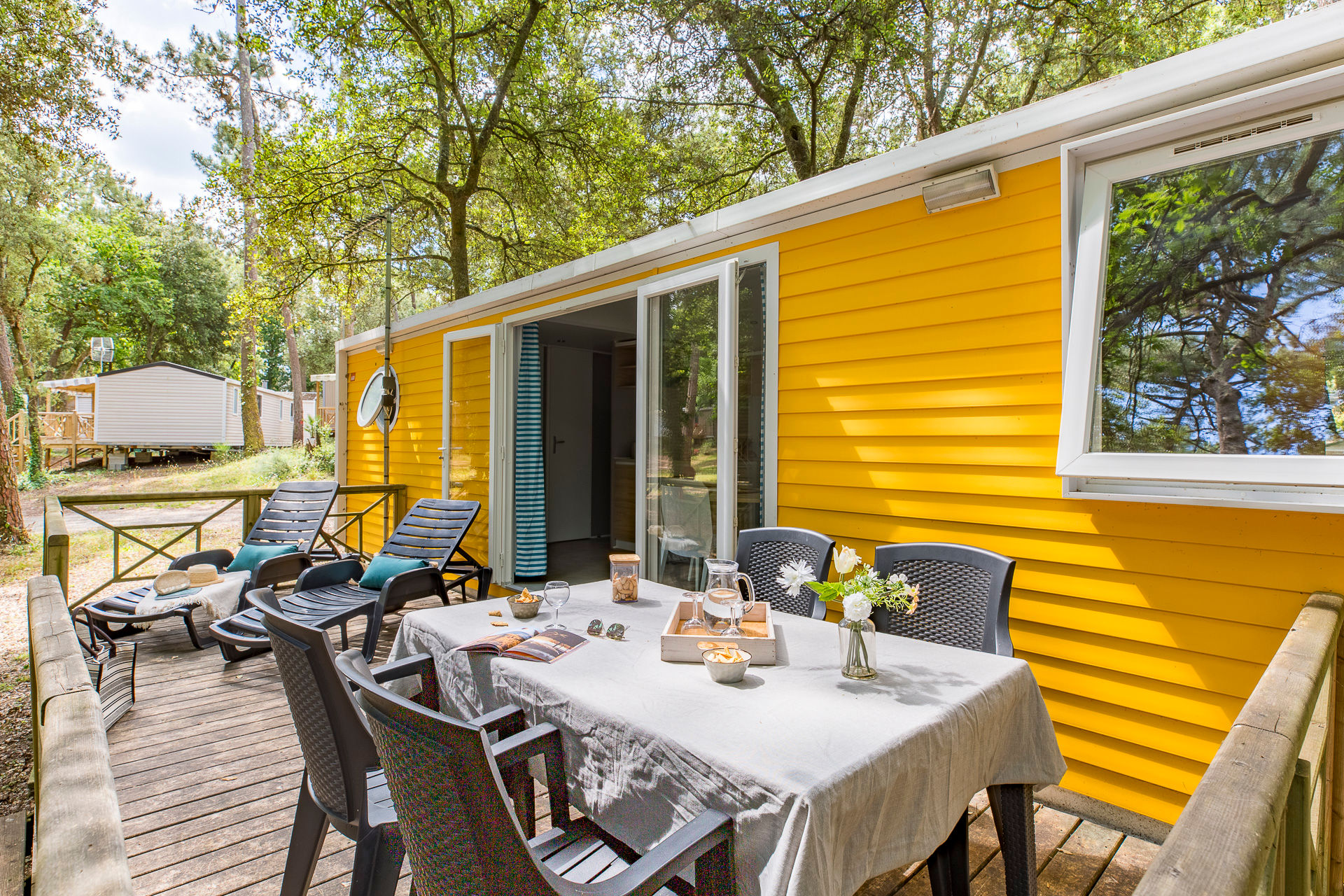 image This vibrant yellow mobile home boasts a spacious outdoor terrace, perfect for enjoying coastal breezes and outdoor dining amidst a serene wooded setting.