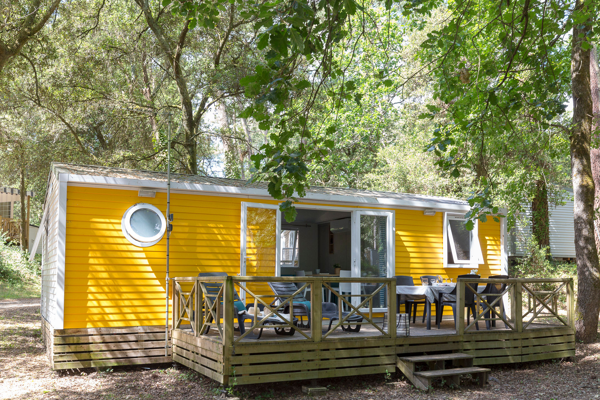 image The vibrant yellow mobile home boasts a charming wooden terrace, perfect for enjoying meals outdoors in the serene surroundings of Camping le Logis.
