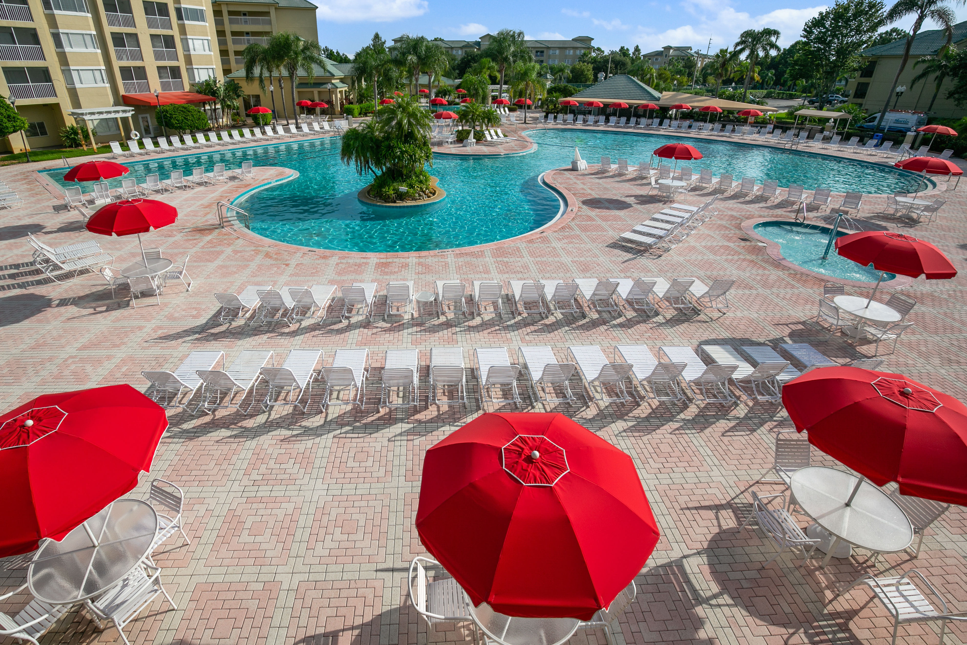 image Bright red umbrellas offer shade around the inviting resort pool area.