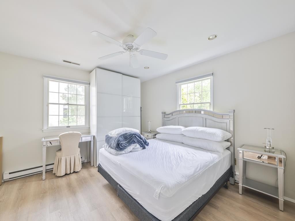 image Bright bedroom featuring a sleek bed frame, plush bedding, a small desk, and large sunlit windows.