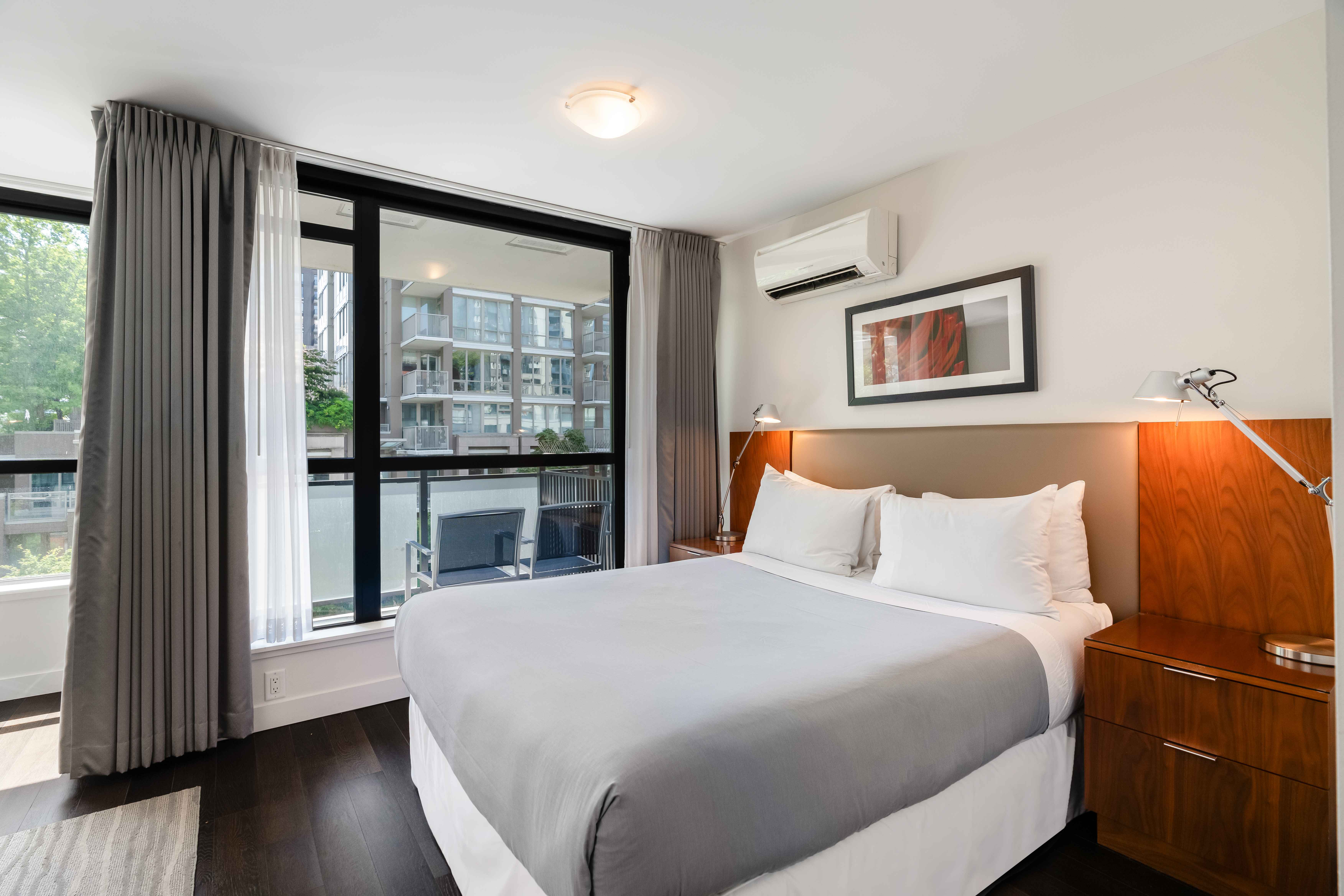 image Spacious bedroom featuring a plush king bed, warm wood accents, and large windows overlooking the city.