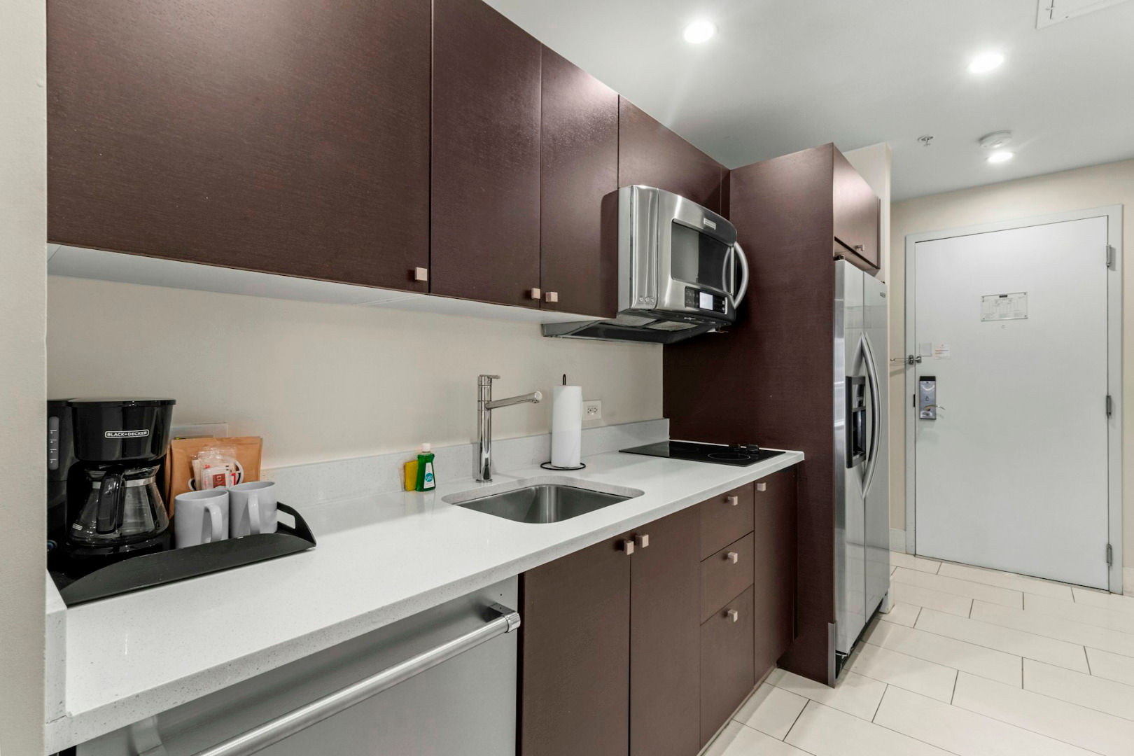 image Contemporary kitchenette with modern cabinetry, sink, microwave, and essential appliances for convenient in-room dining.