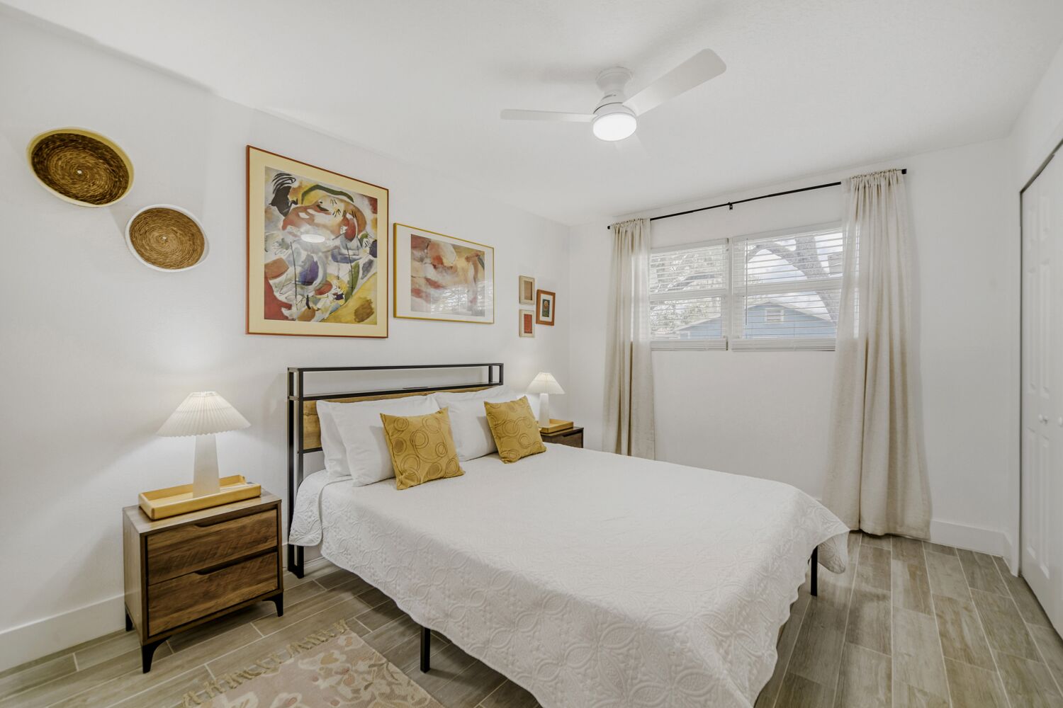 image The inviting bedroom boasts a soft white quilt, decorative pillows, and vibrant artwork, along with a warm ambience created by soft lighting from stylish bedside lamps.