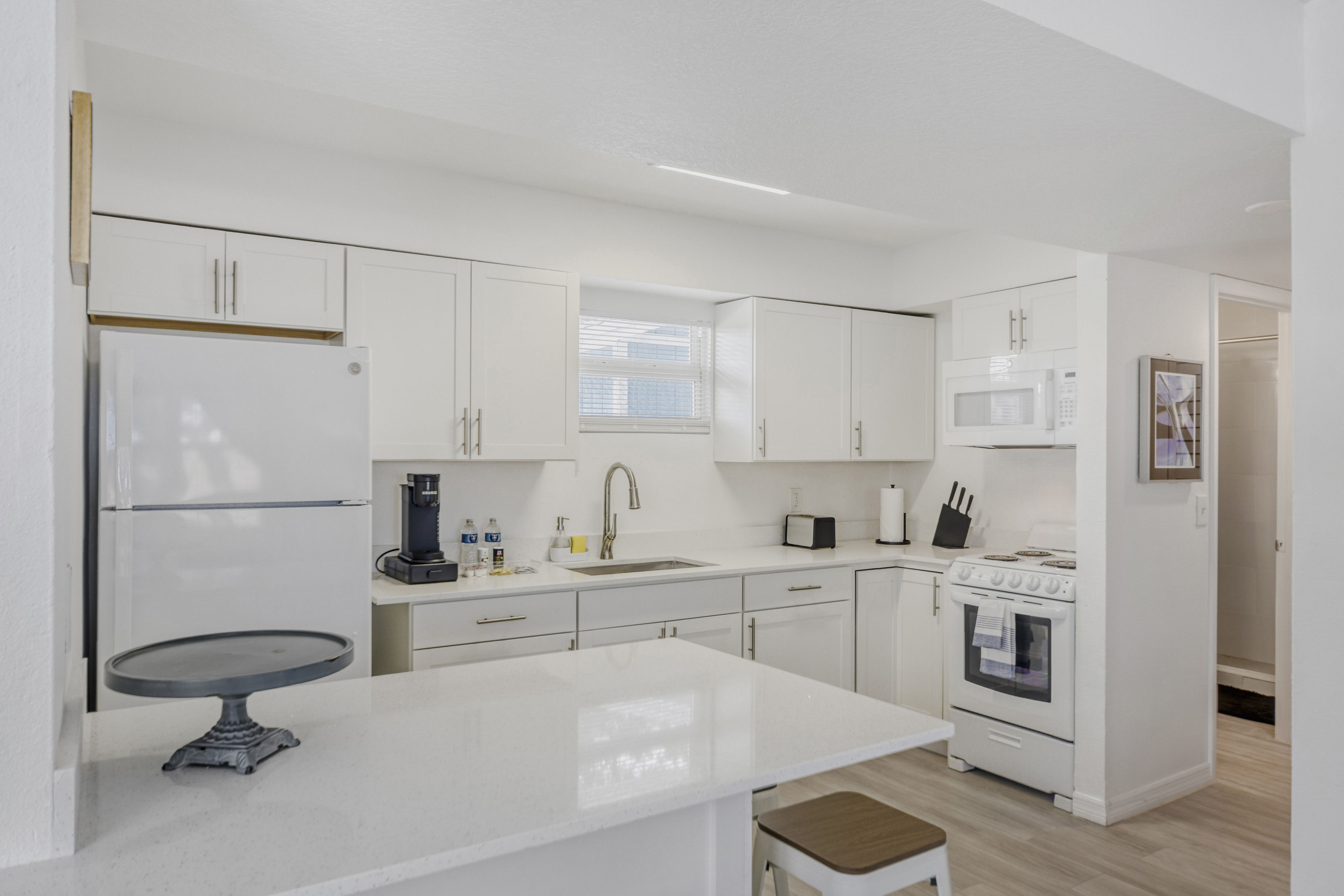 image Bright modern kitchenette with white cabinetry, full-size appliances, and a spacious island counter.