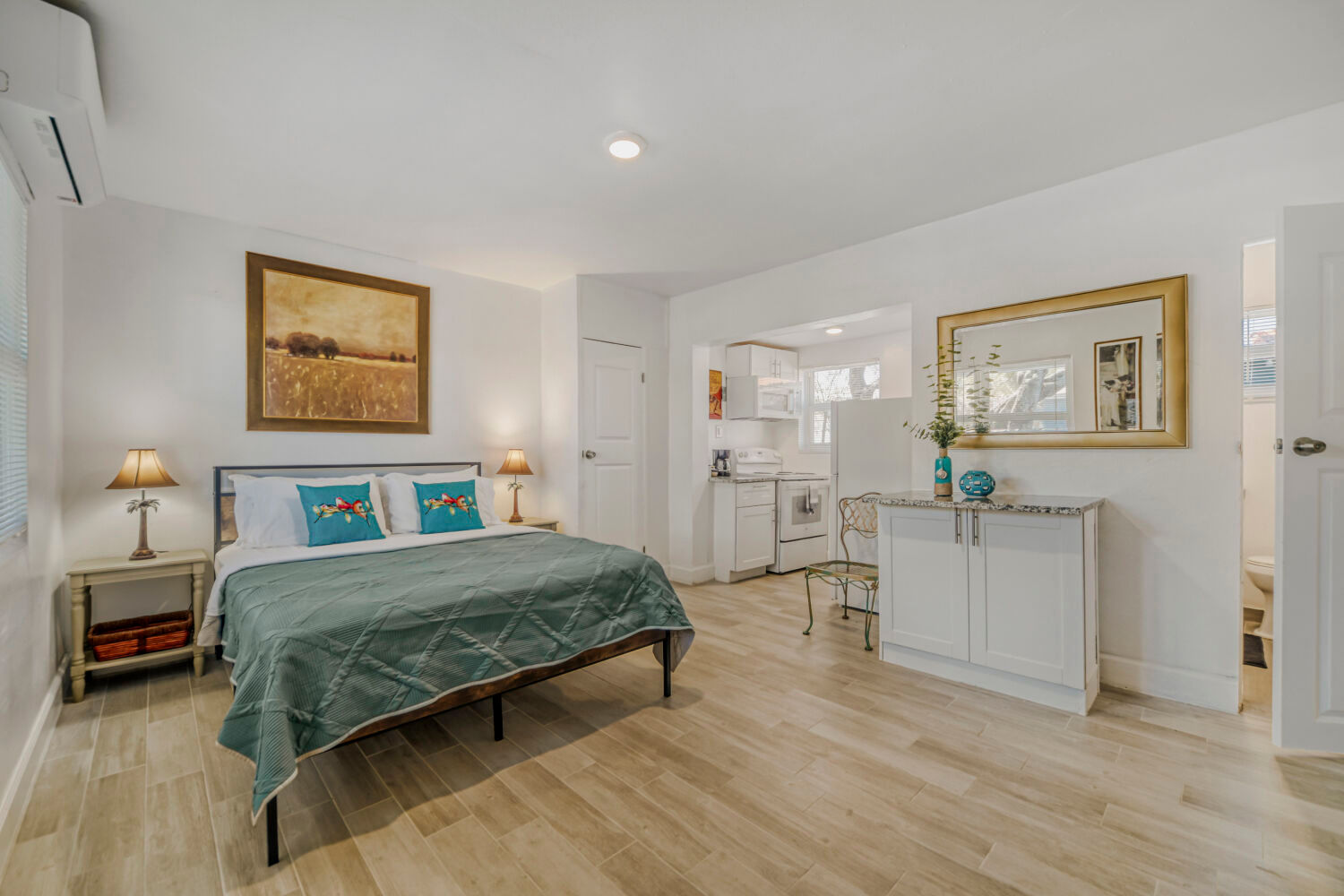 image Queen bed with bedside table and lamp in a bright, simply furnished studio layout.