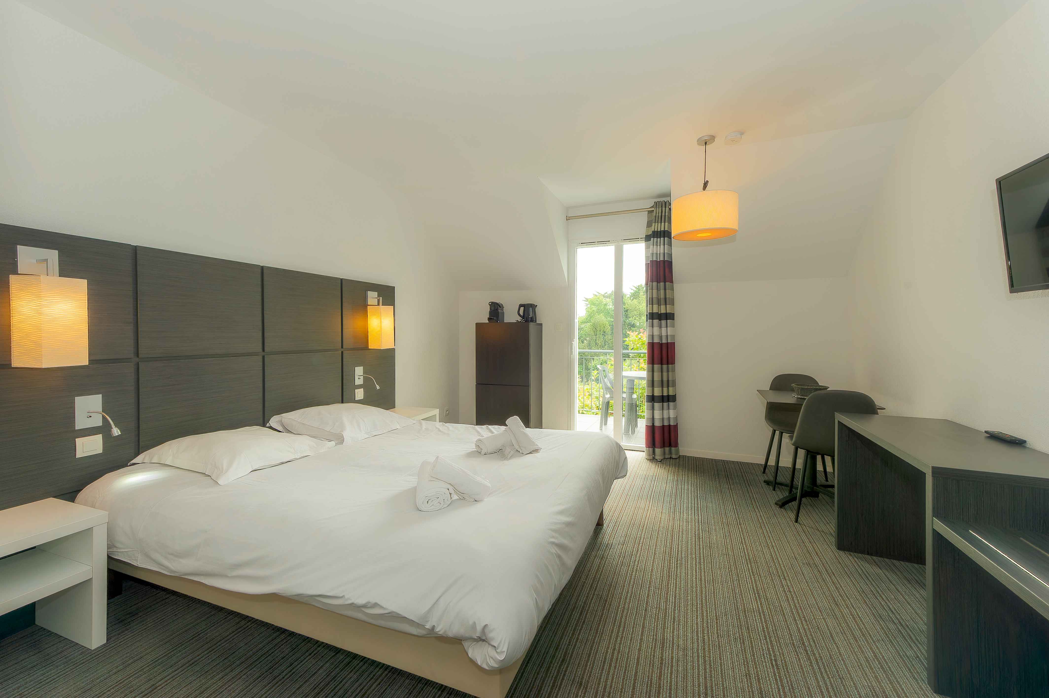 image Double bed with white linens, wall-mounted TV, and a large window looking onto the park — wake up to green views in Pont-Aven.