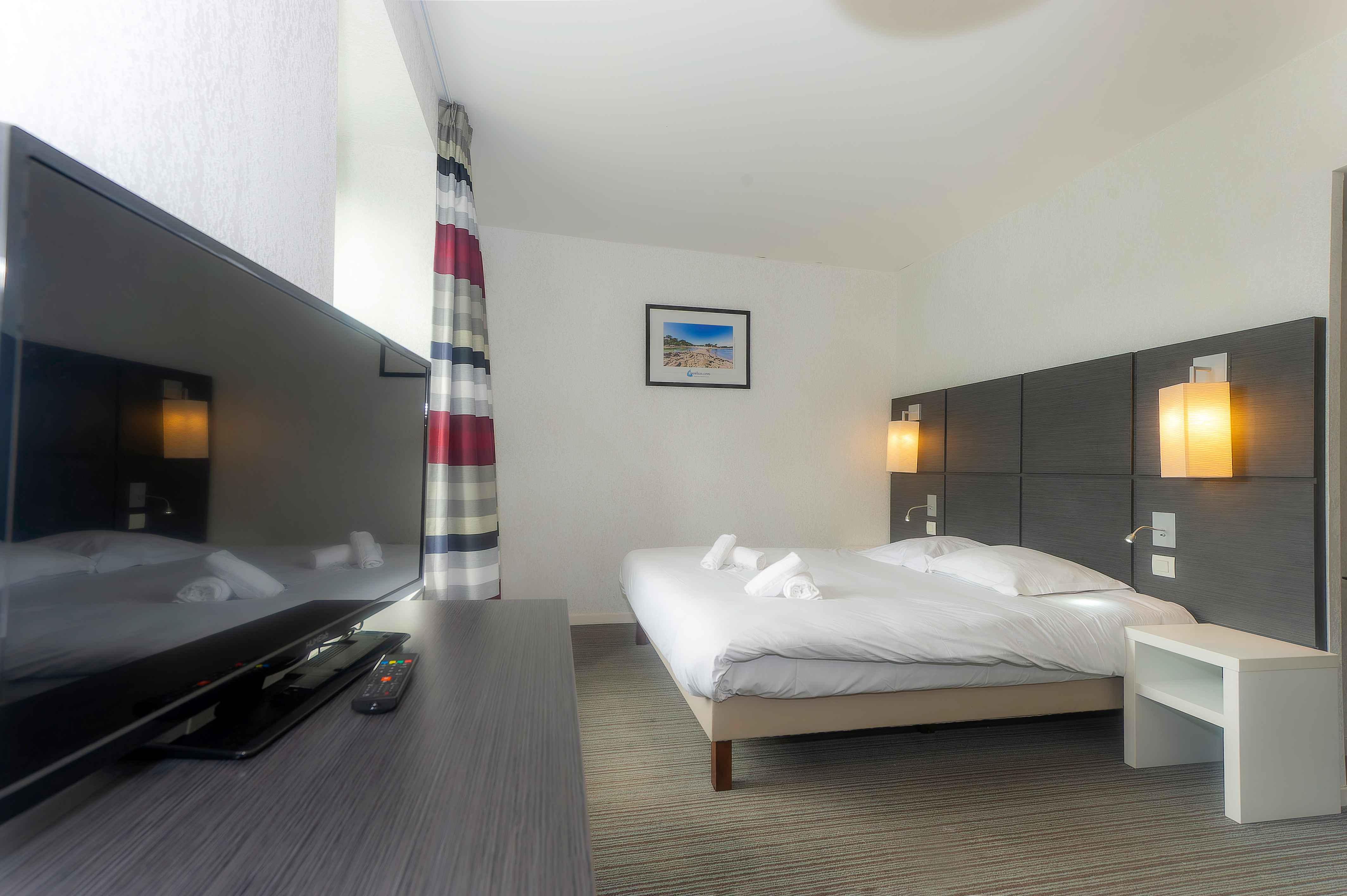 image Double bed with white linens and warm pendant lighting, set against dark grey wall panels — air conditioning keeps things cool in summer.