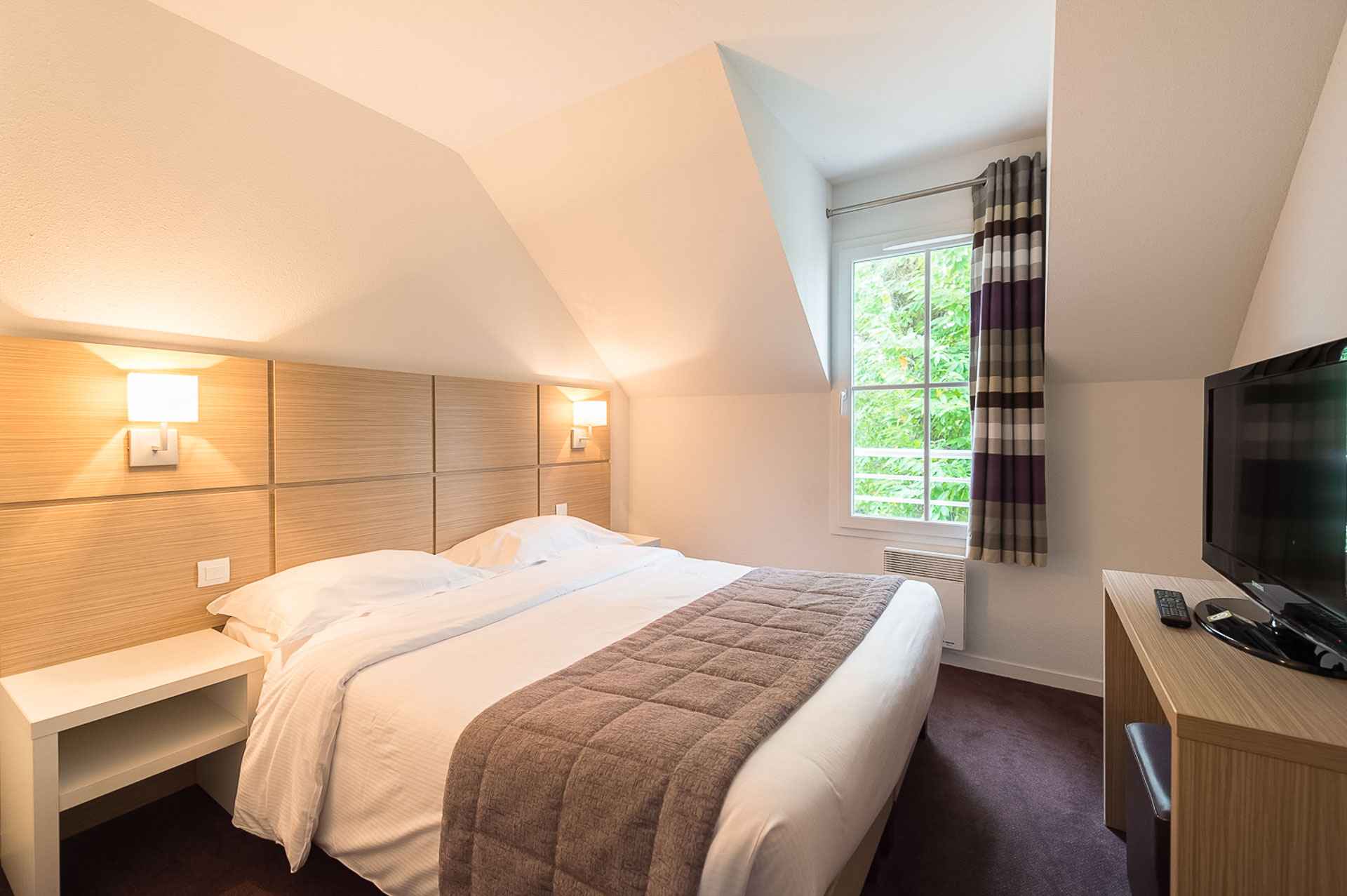 image Double bed with warm bedside lighting and an arched ceiling — the bedroom in this garden-level apartment above Pont-Aven.