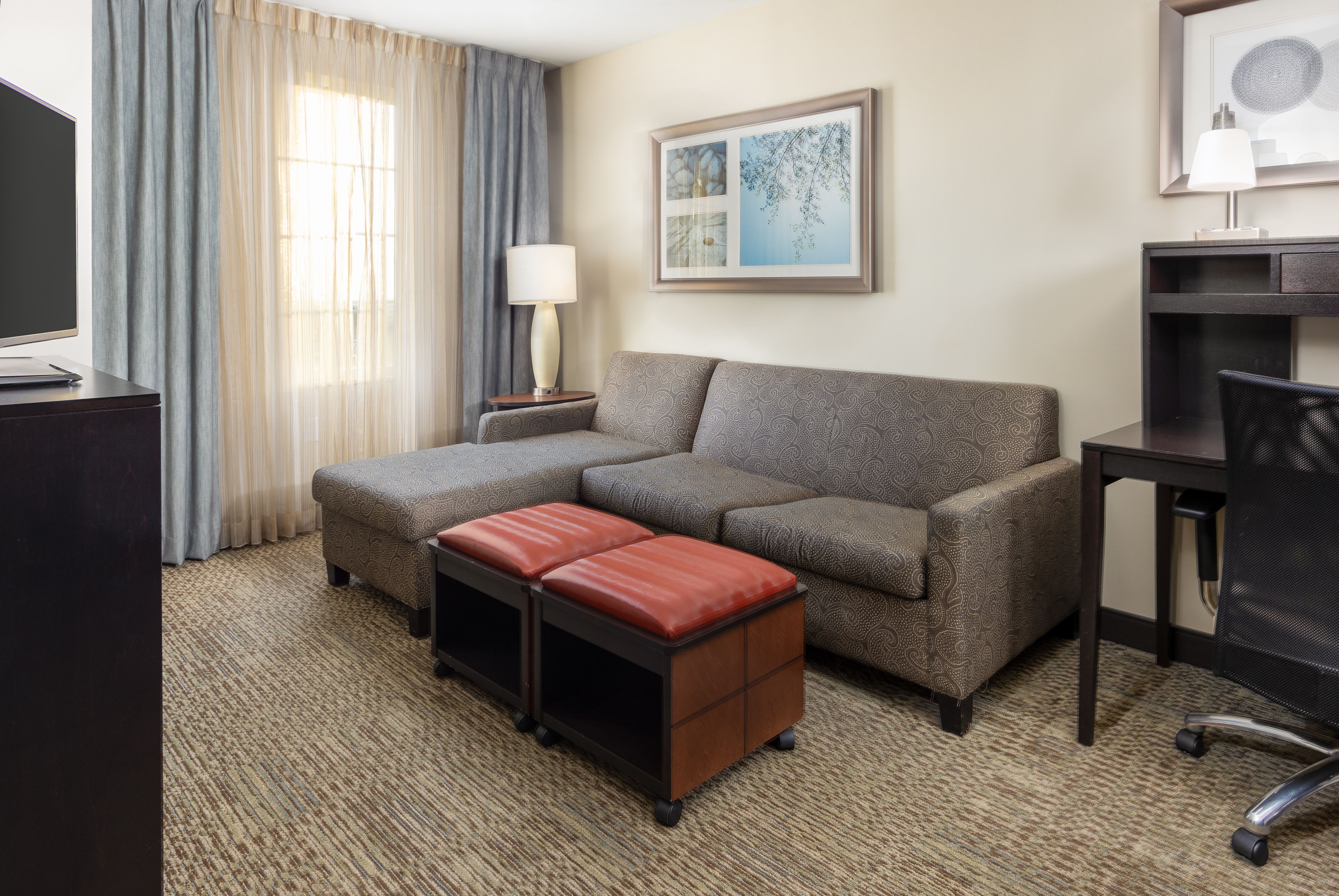 image Spacious living area with sofa, ottoman, lamp, and desk.