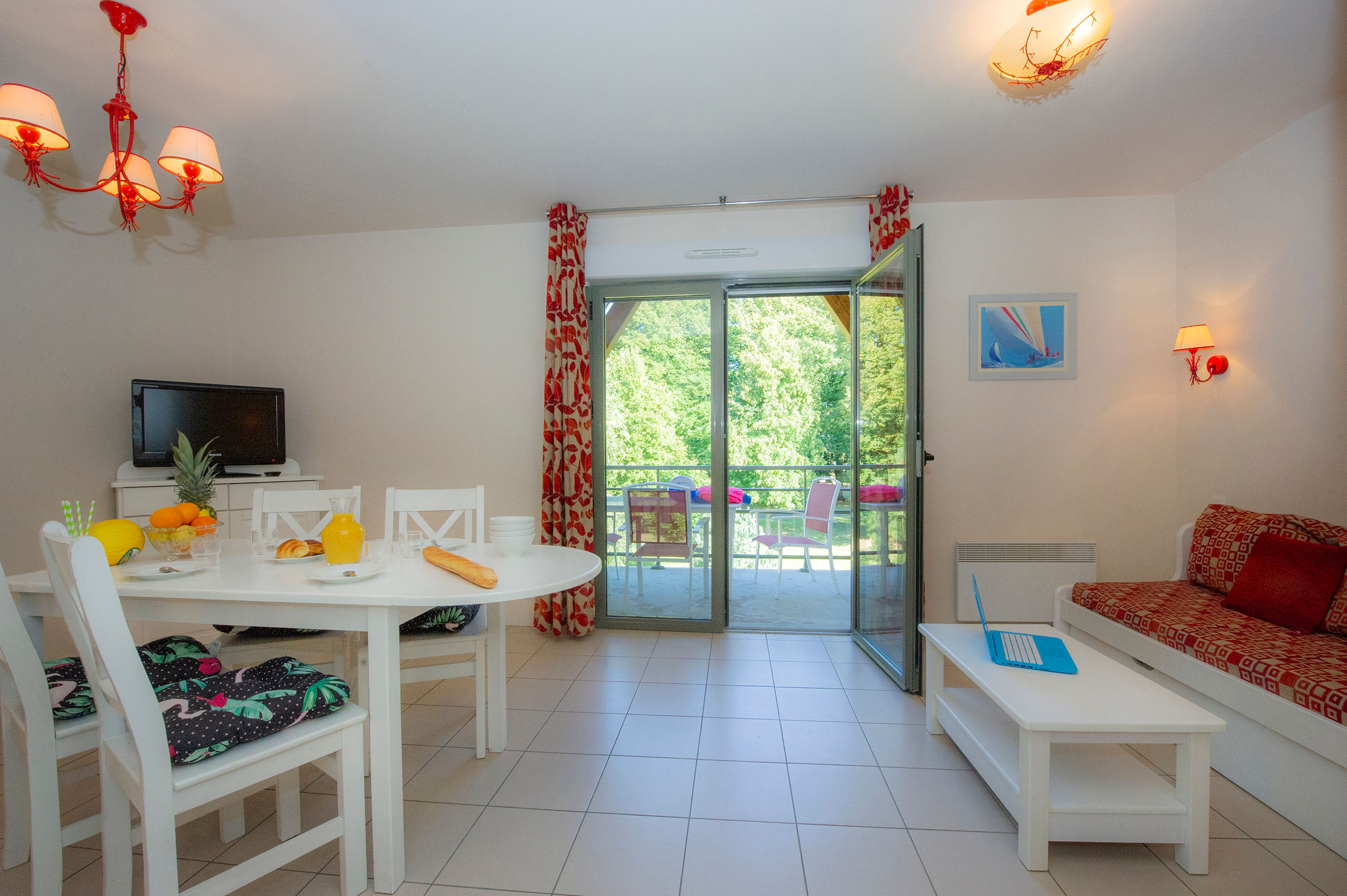 image Open-plan living and dining area with round white table, four seats, wall-mounted TV, and sliding doors to the balcony