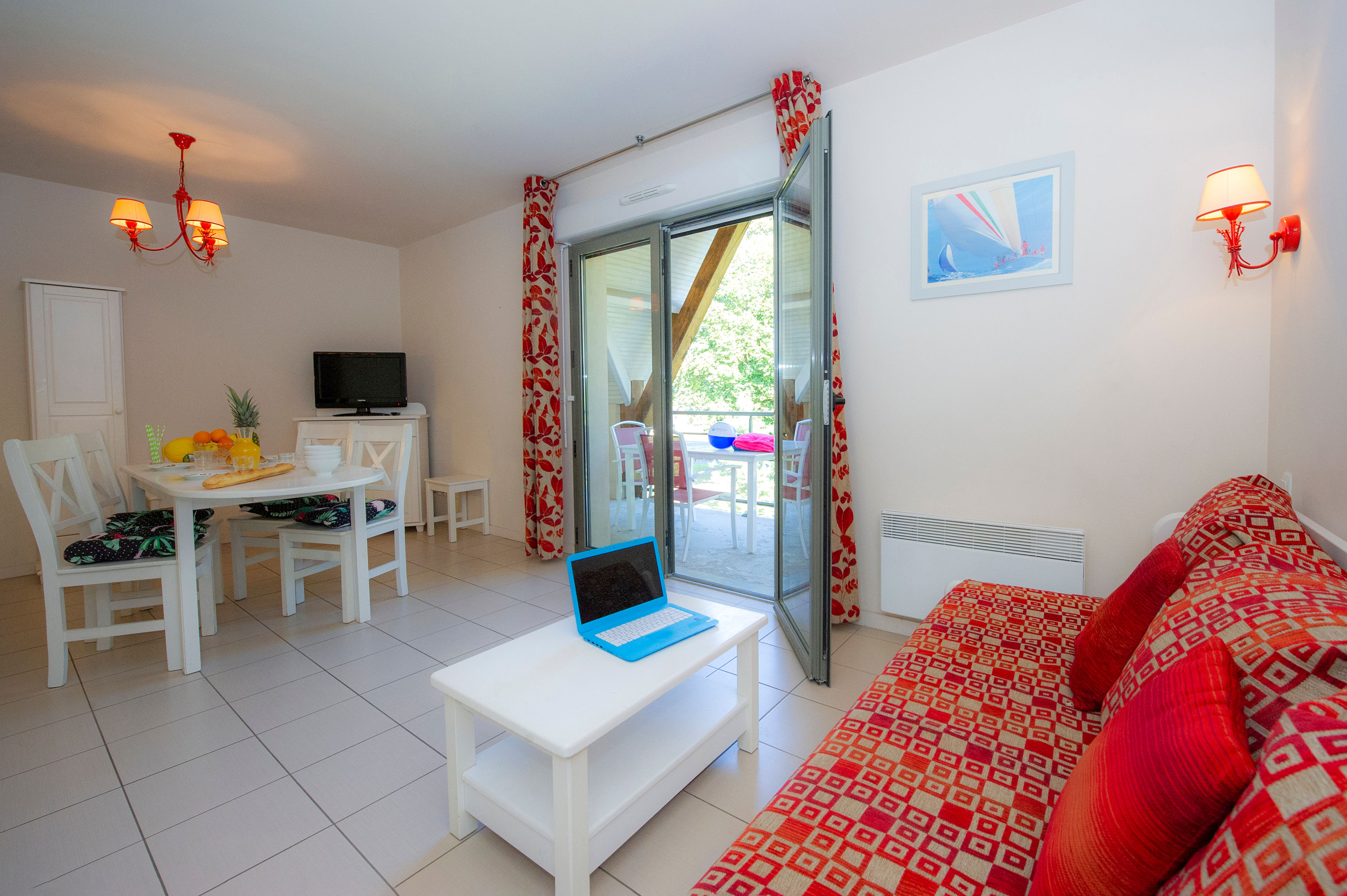 image Open-plan living and dining with red sofa, wall-mounted TV, and glass doors opening to the furnished balcony