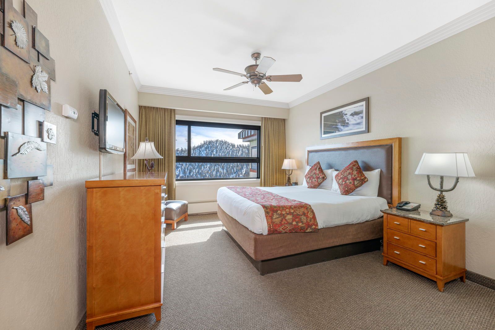 image Wake up to snow-dusted pines seen through the window, with a king bed, ceiling fan, wall-mounted TV, and pine dresser all within reach.