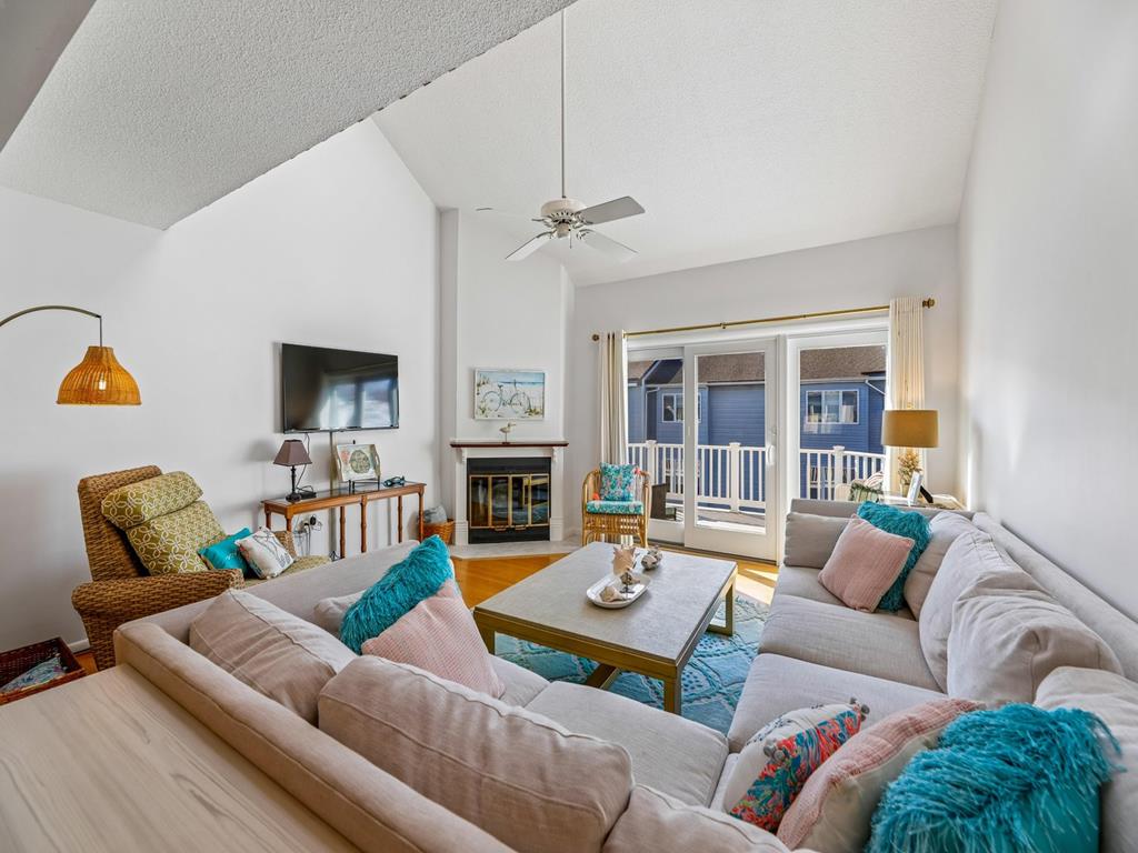 image Living room with a ceiling fan, L-shaped sectional sofa, colourful cushions, and a flat-screen TV on the wall
