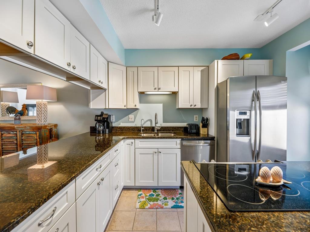 image Kitchen with white cabinetry, dark granite countertops, stainless steel fridge, and a colourful floor mat