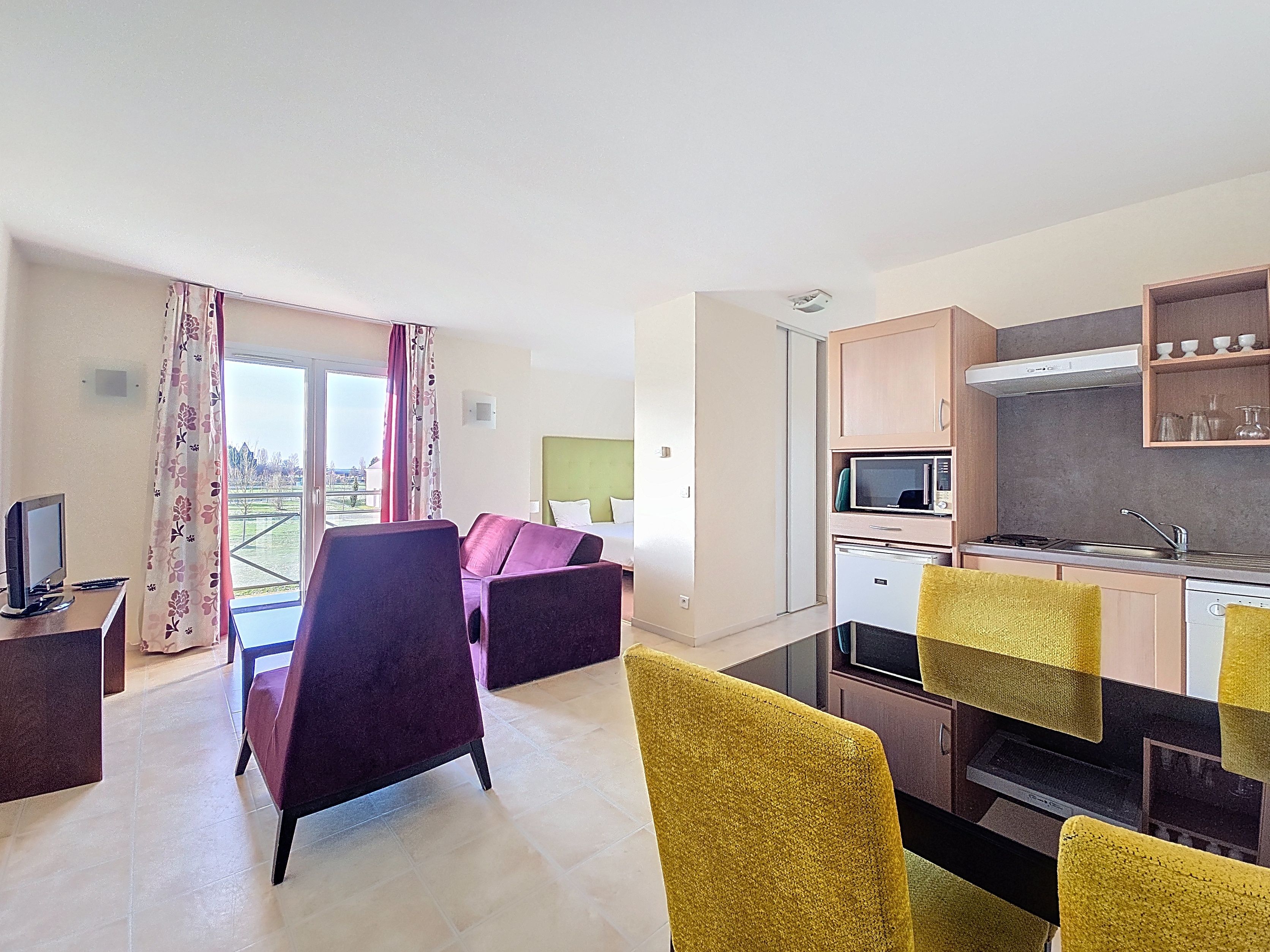 image Kitchenette with light wood cabinetry, electric hob, microwave, and yellow chairs around a black dining table