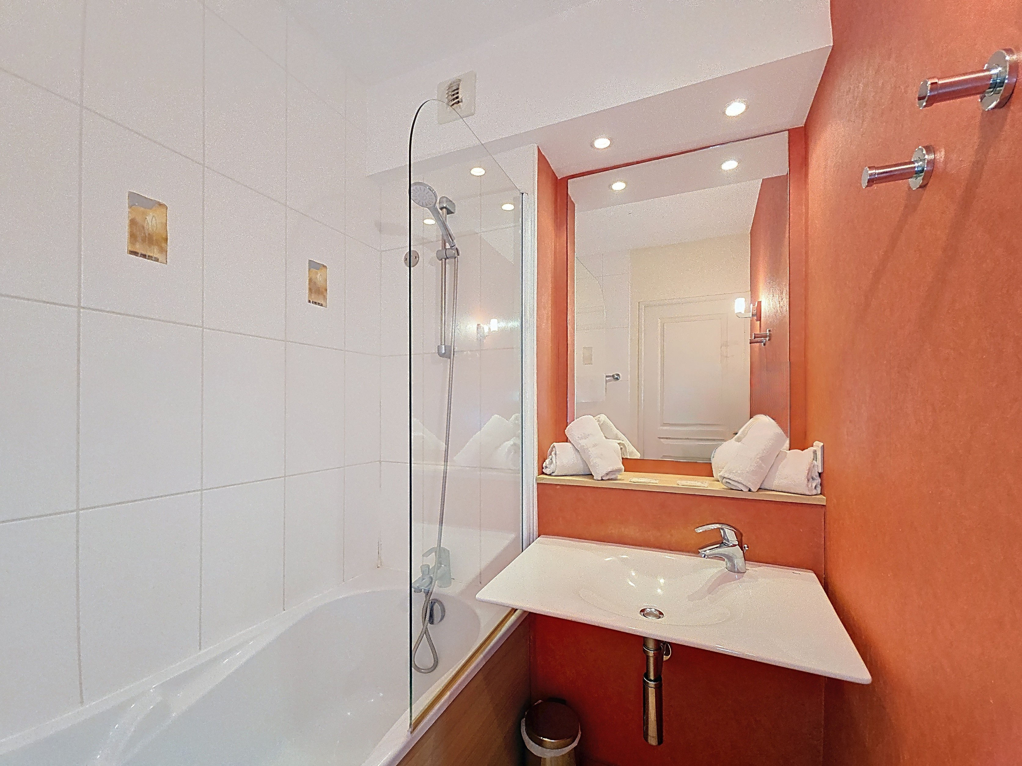 image Bathroom with a white-tiled bathtub and shower attachment, basin, and towels on display