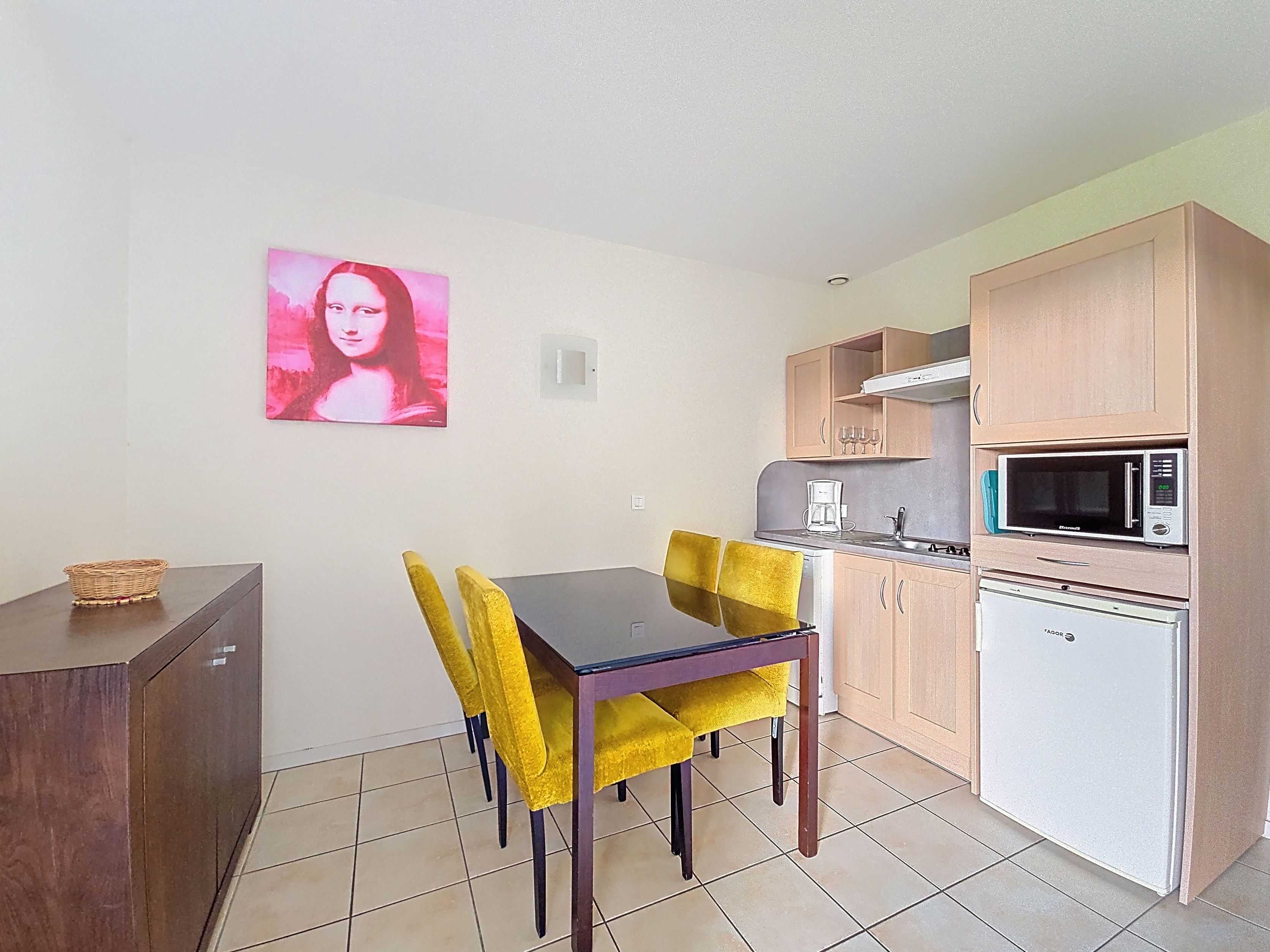 image Kitchenette with light wood cabinetry, yellow dining chairs, and a pink artwork print on the wall