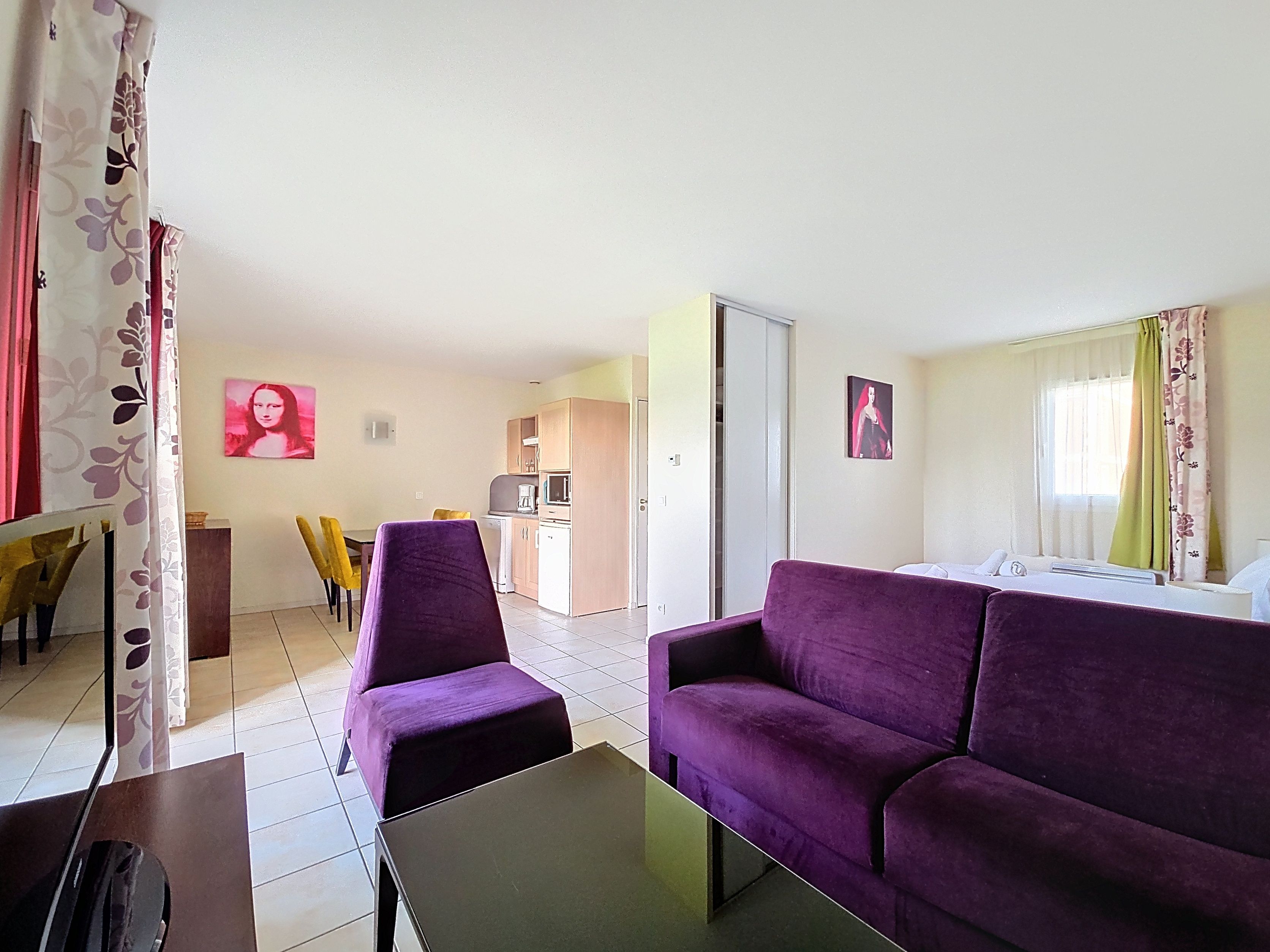 image Open-plan layout combines dining area and kitchenette — purple sofa and colourful artwork visible throughout