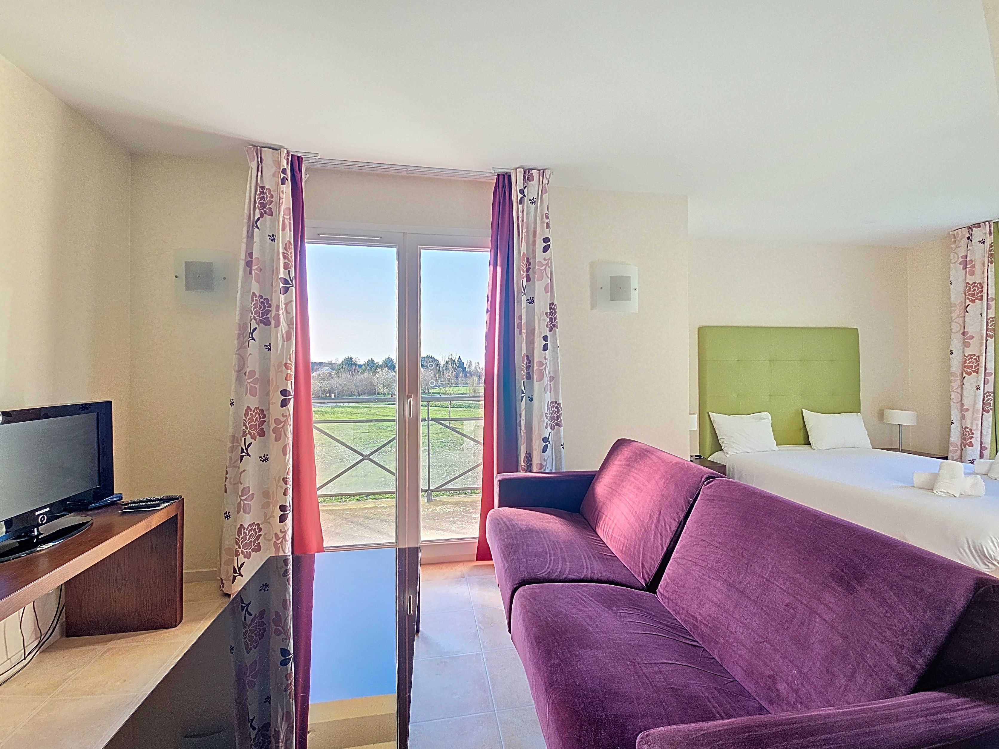 image Studio with two single beds, purple sofa, TV, and large windows with floral curtains looking onto garden